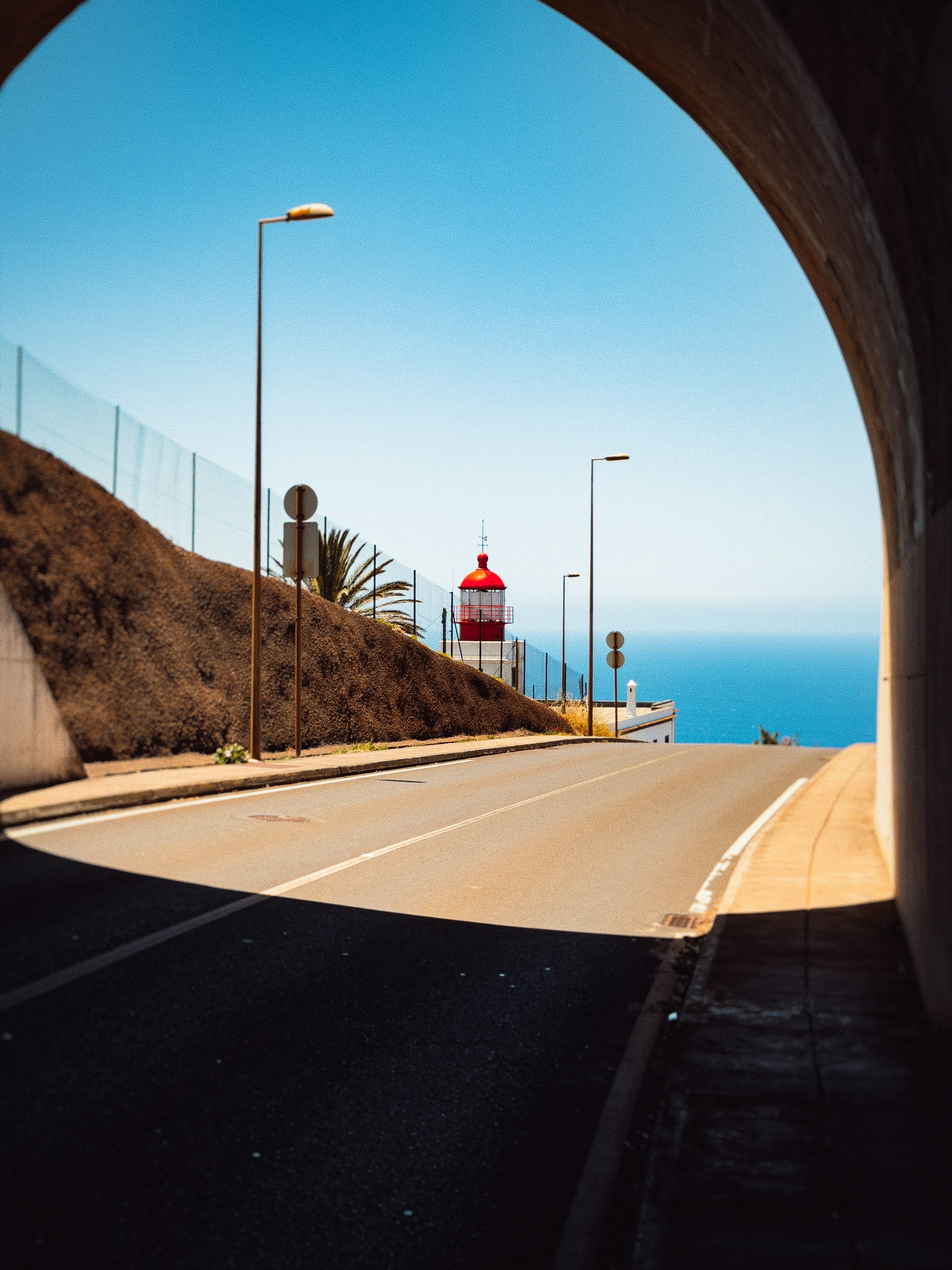 Road leading to a red lighthouse and vast blue ocean.