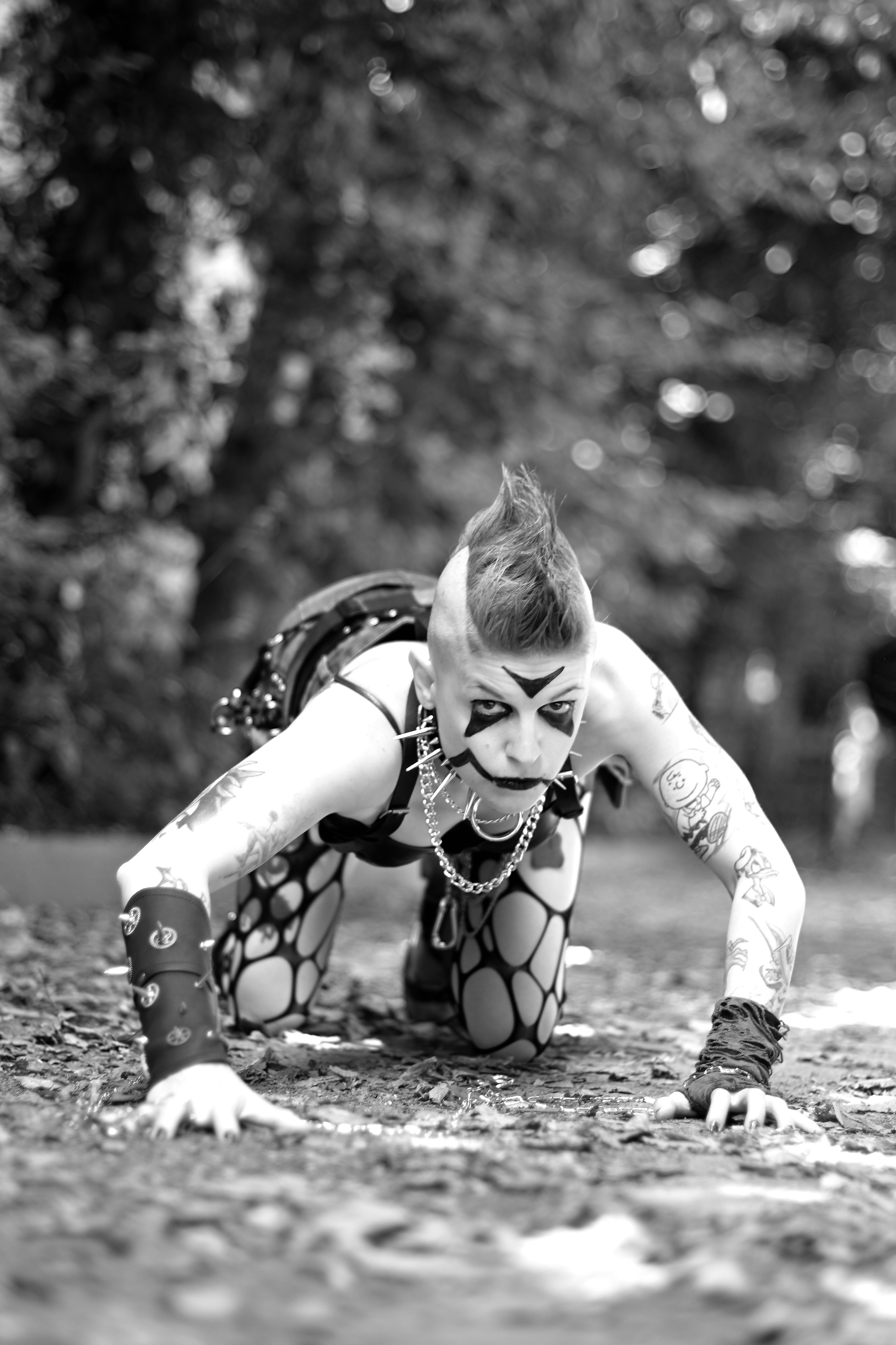 A person with a mohawk and face paint crawling outdoors.