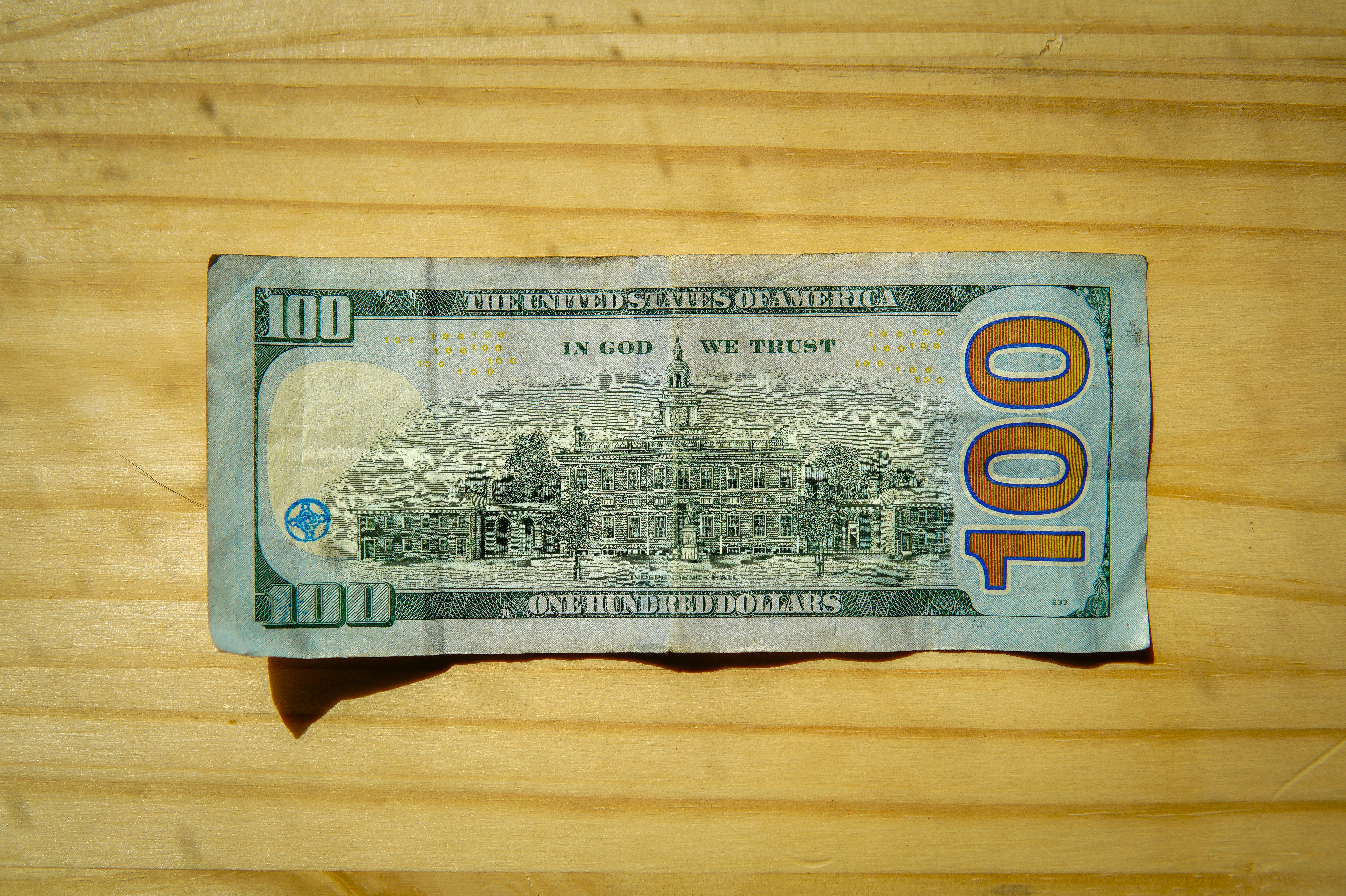 A one hundred dollar bill on a wooden surface.