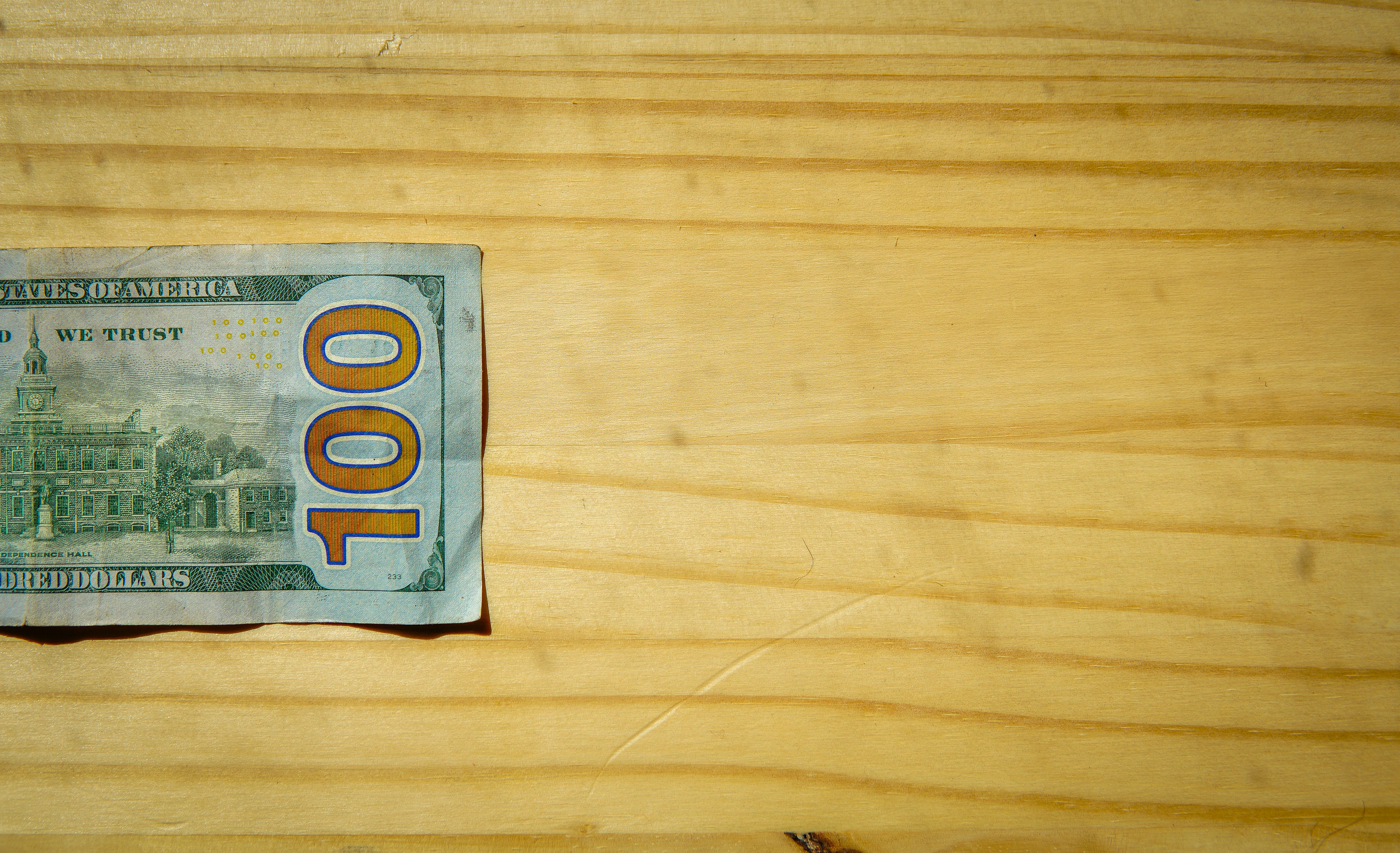 A one hundred dollar bill on a light wooden surface.