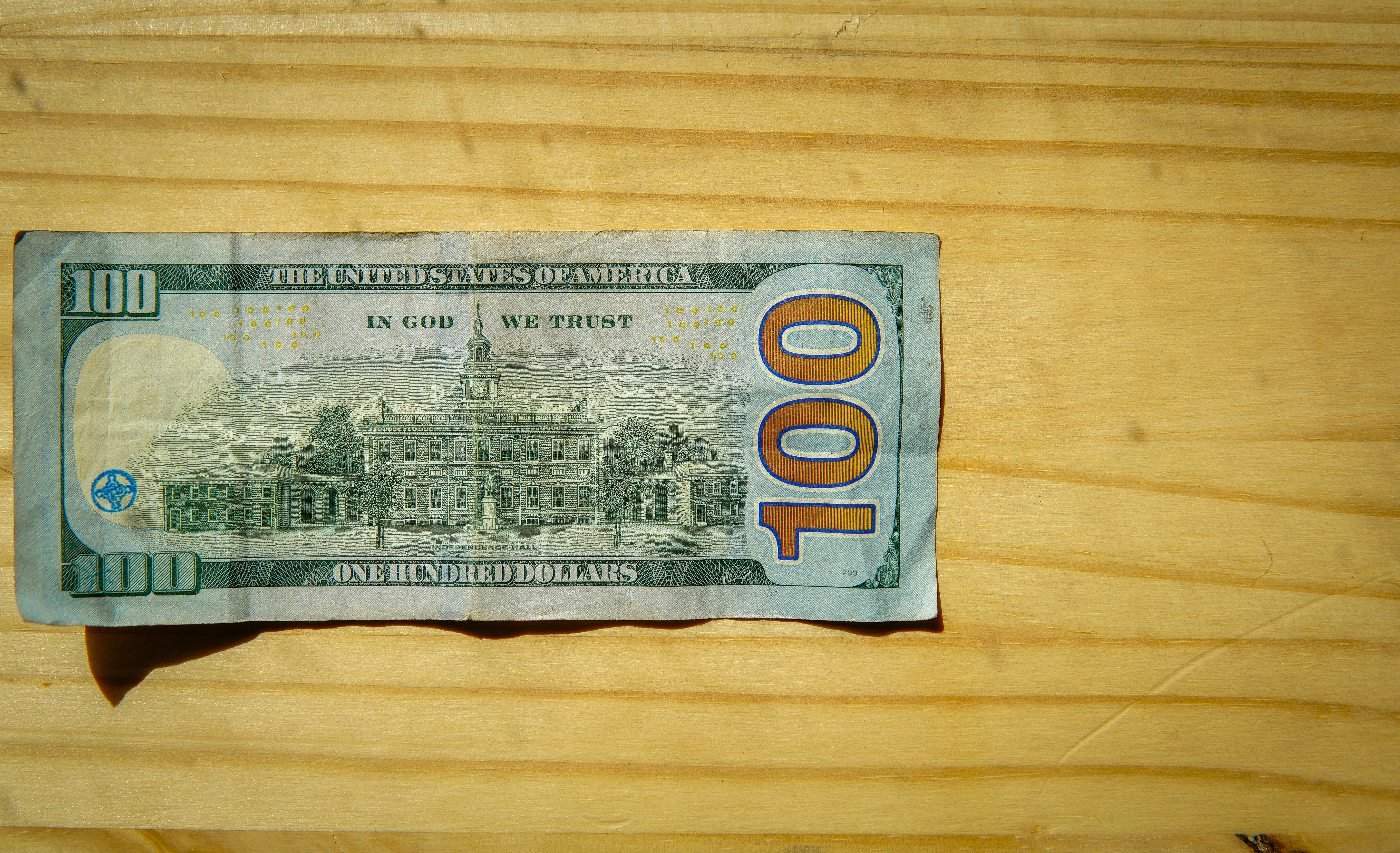 A hundred dollar bill on a wooden surface.