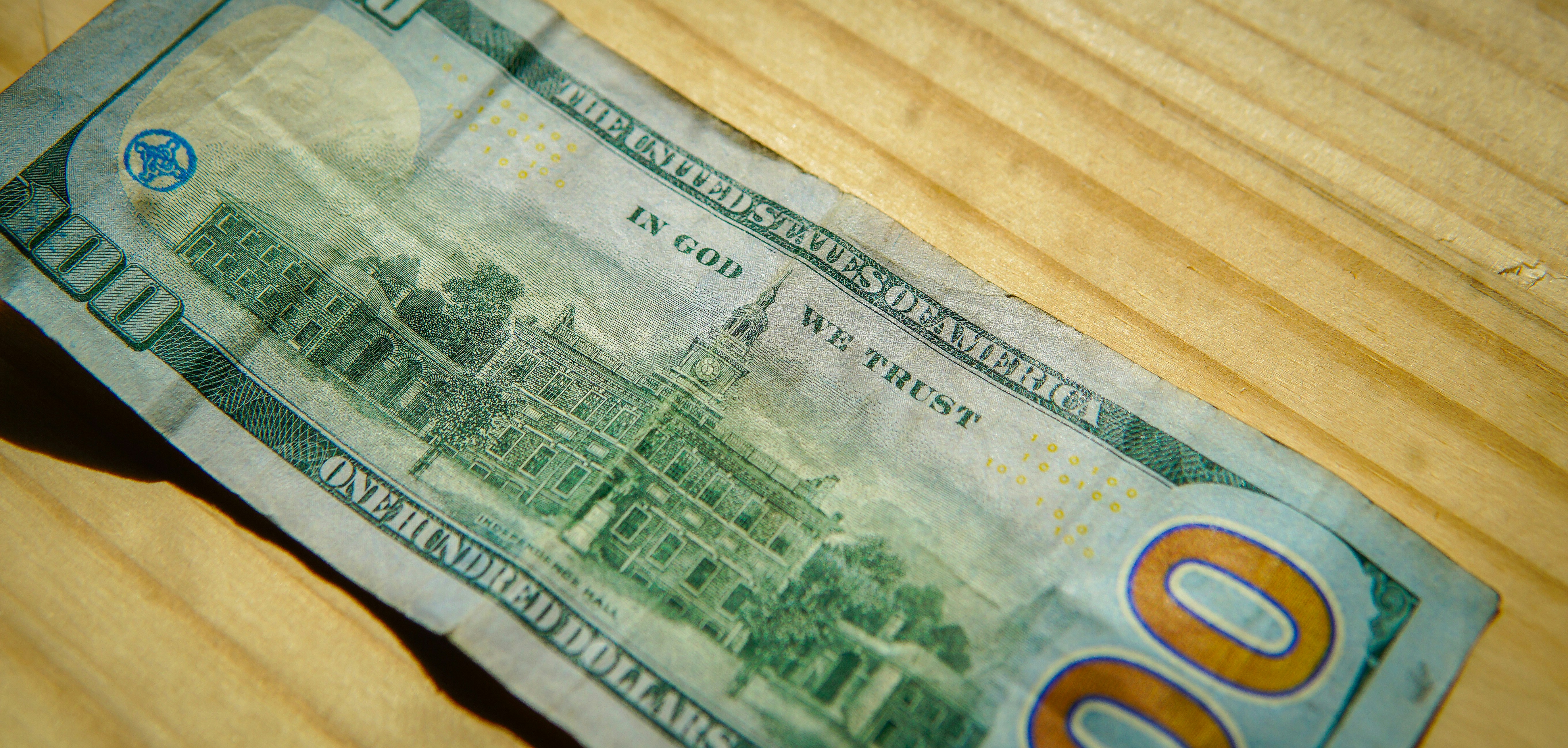A hundred dollar bill on a wooden surface.