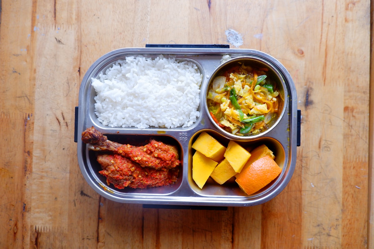 Adult meal-prep bento box with chicken, rice, and fresh vegetables in a partitioned container
