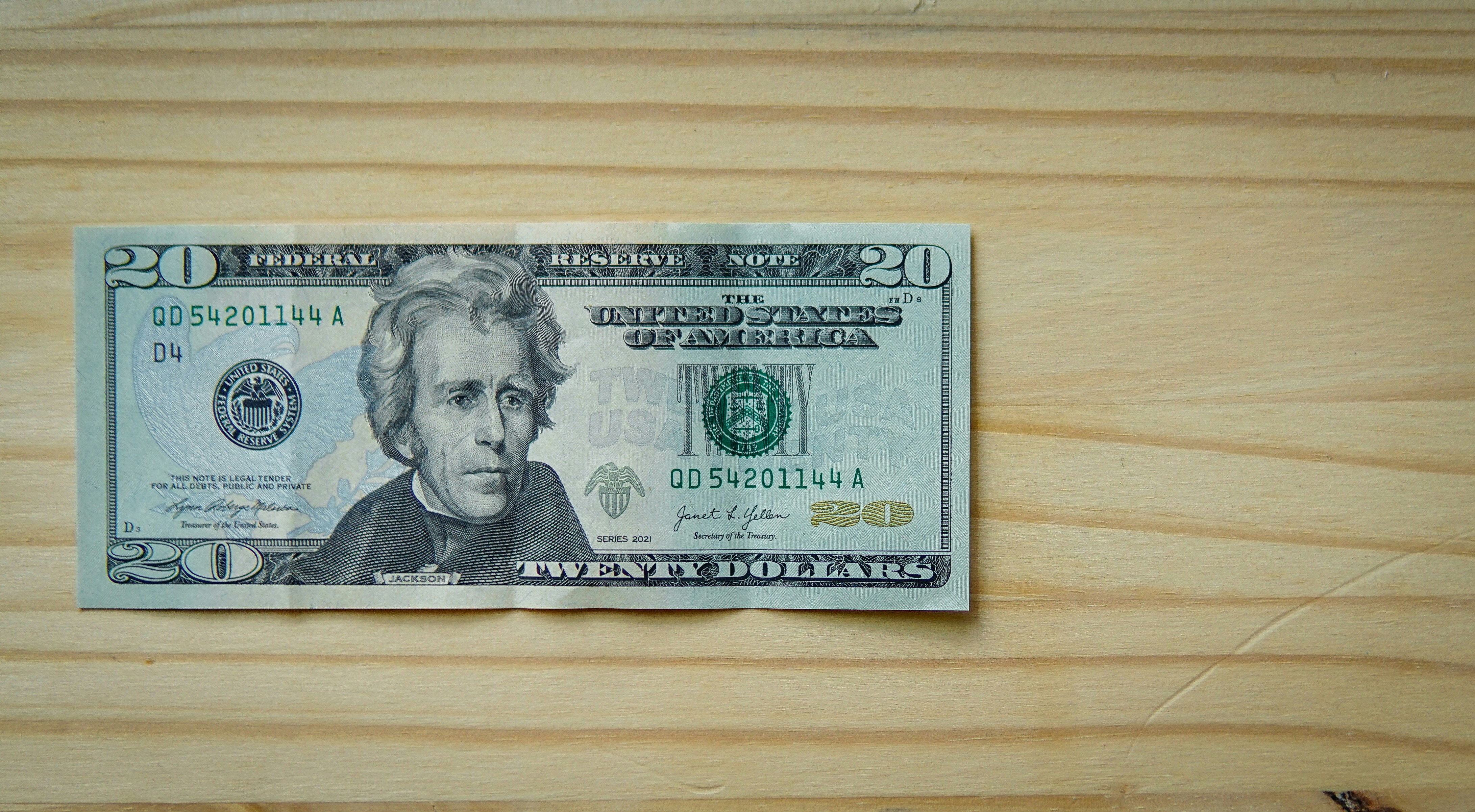 A twenty-dollar bill rests on a light wooden surface.