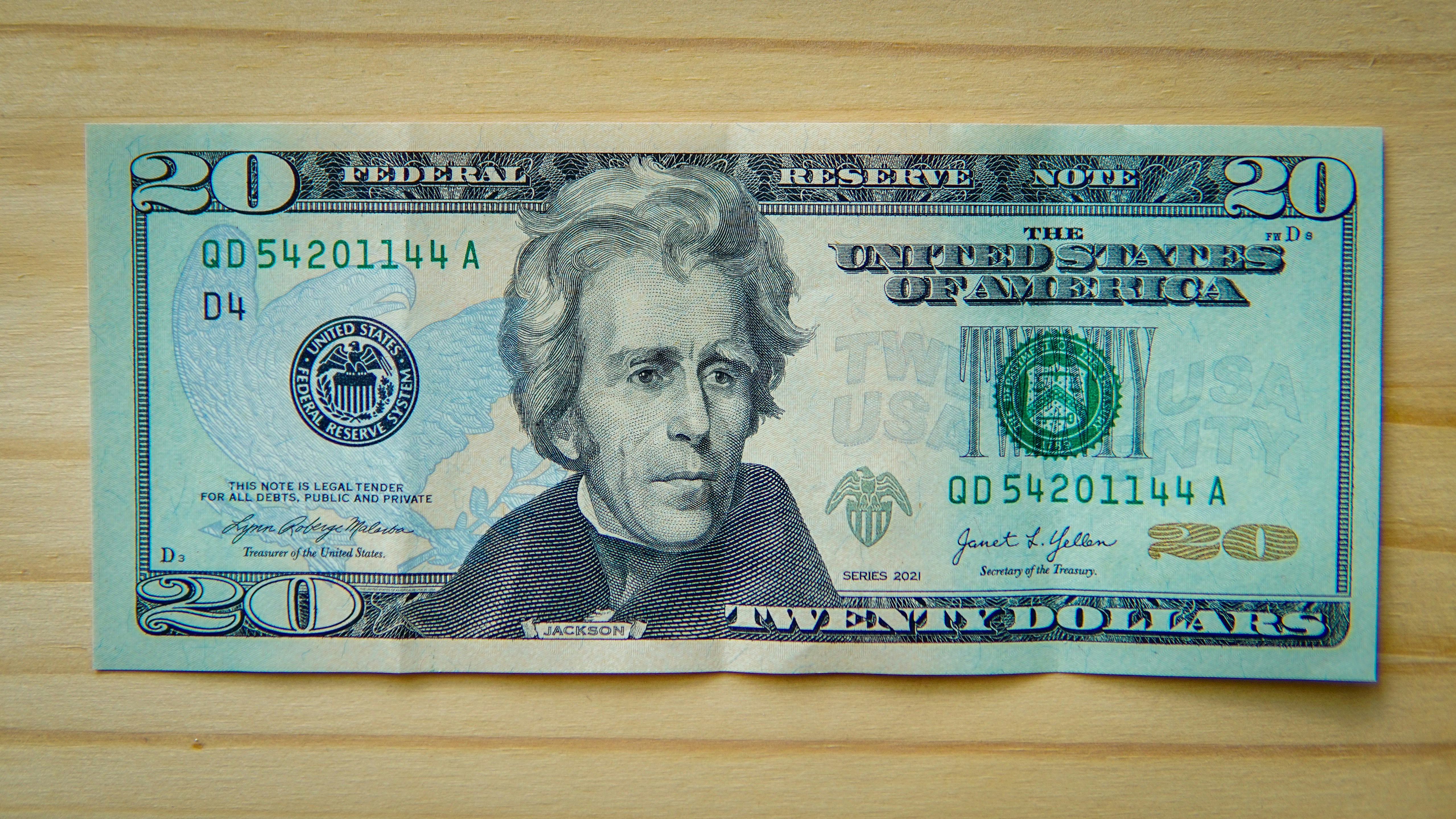 A twenty-dollar bill lying flat on a wooden surface.