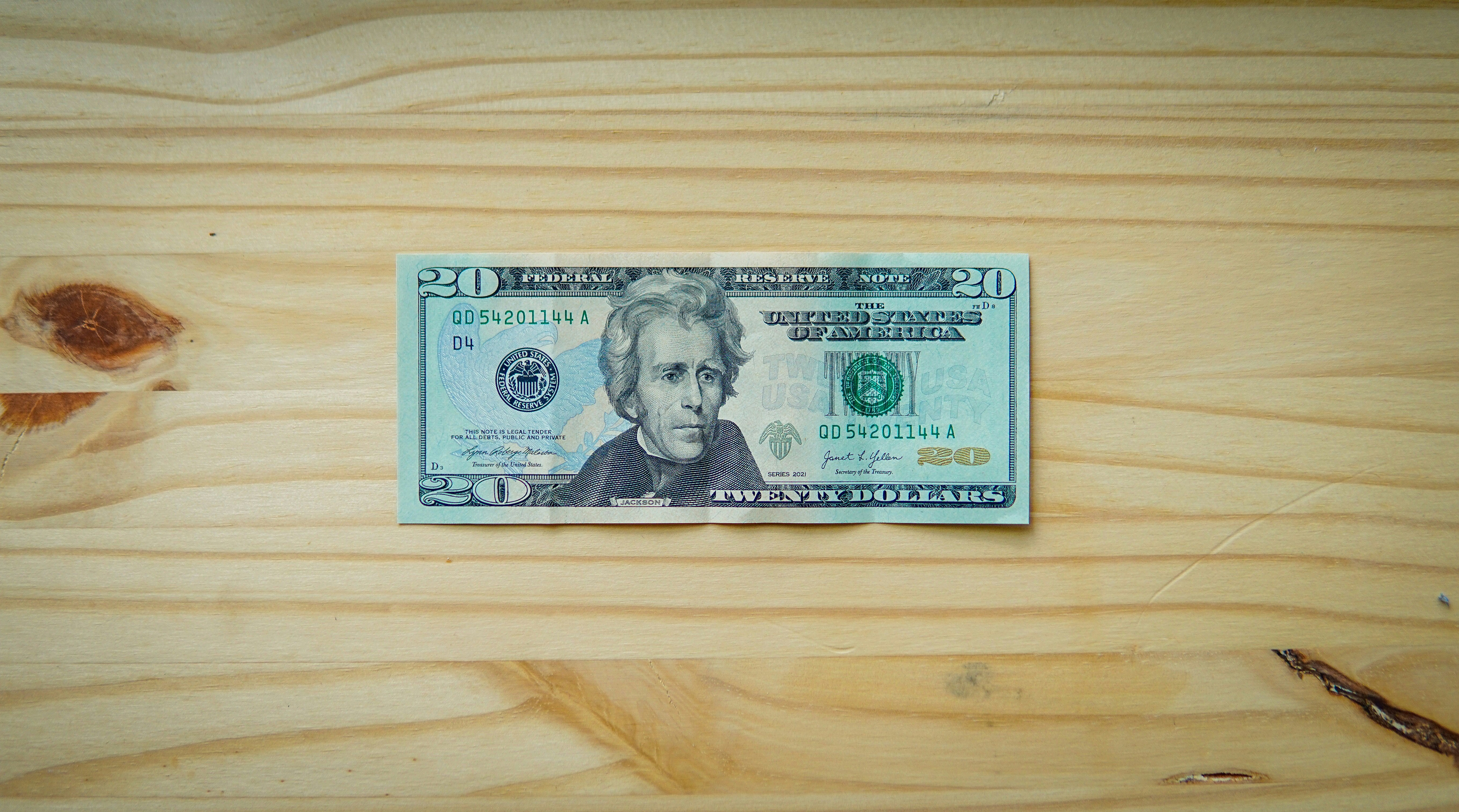 A twenty-dollar bill rests on a light wooden surface.