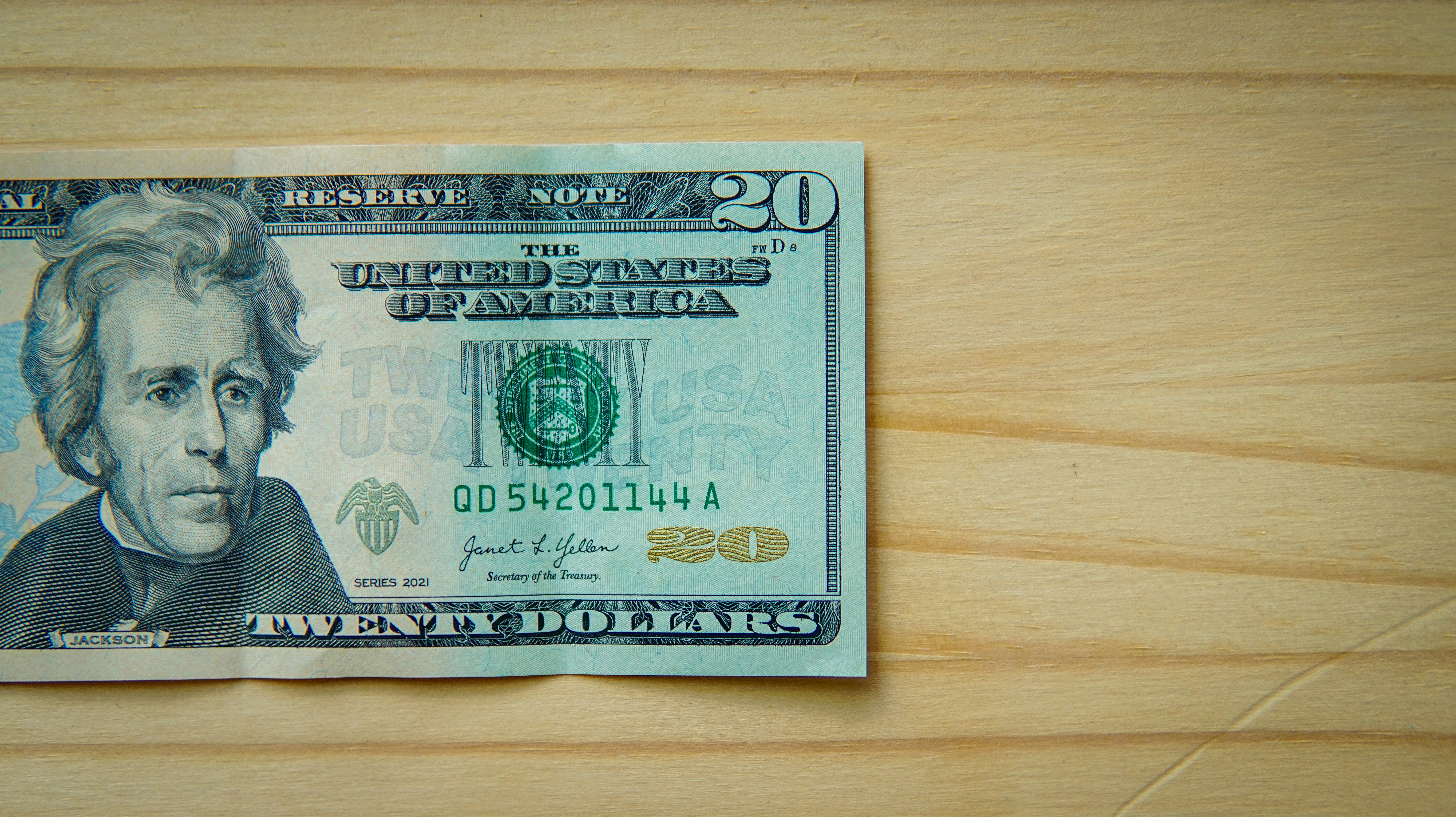 A twenty-dollar bill rests on a light wooden surface.