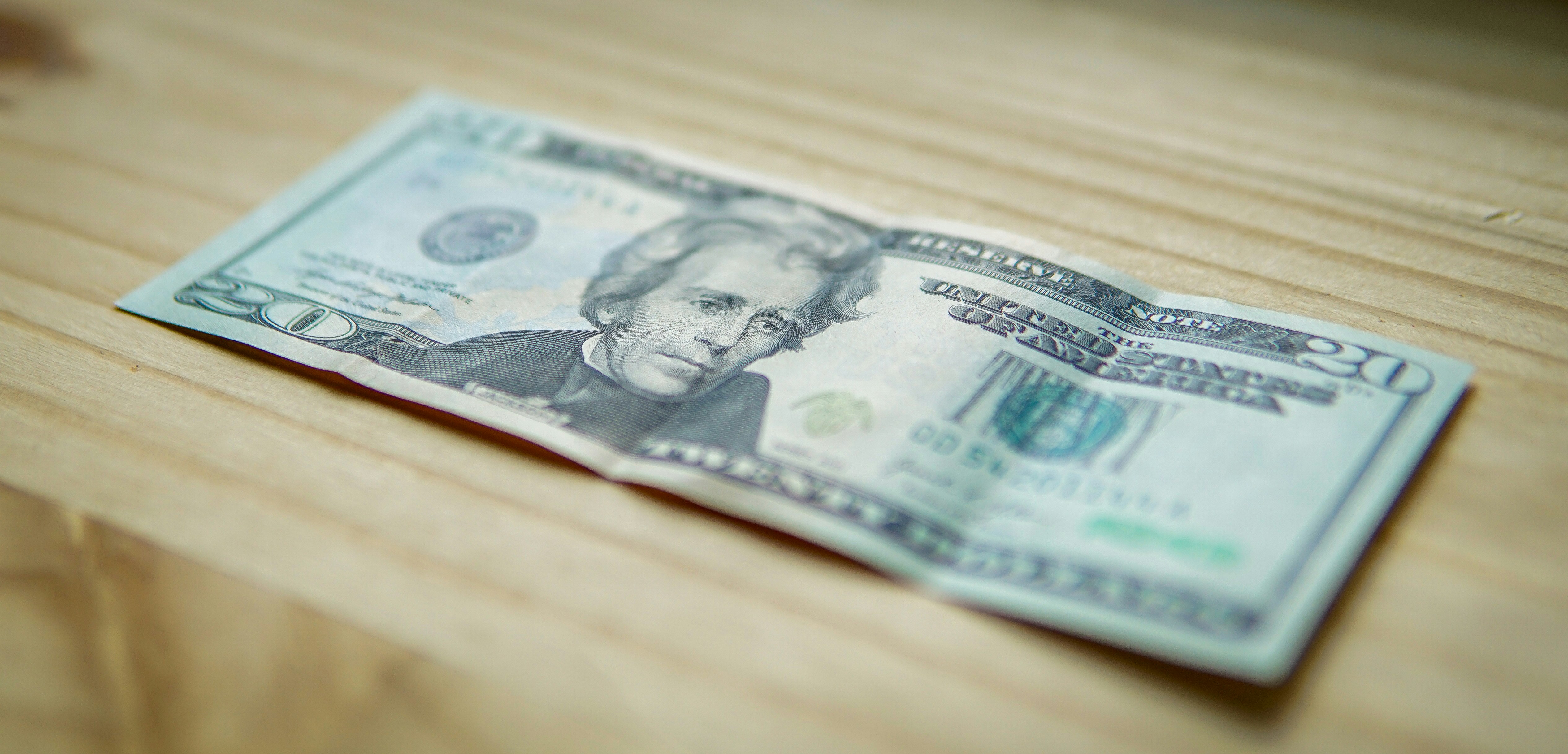 A crumpled twenty-dollar bill on a wooden surface.