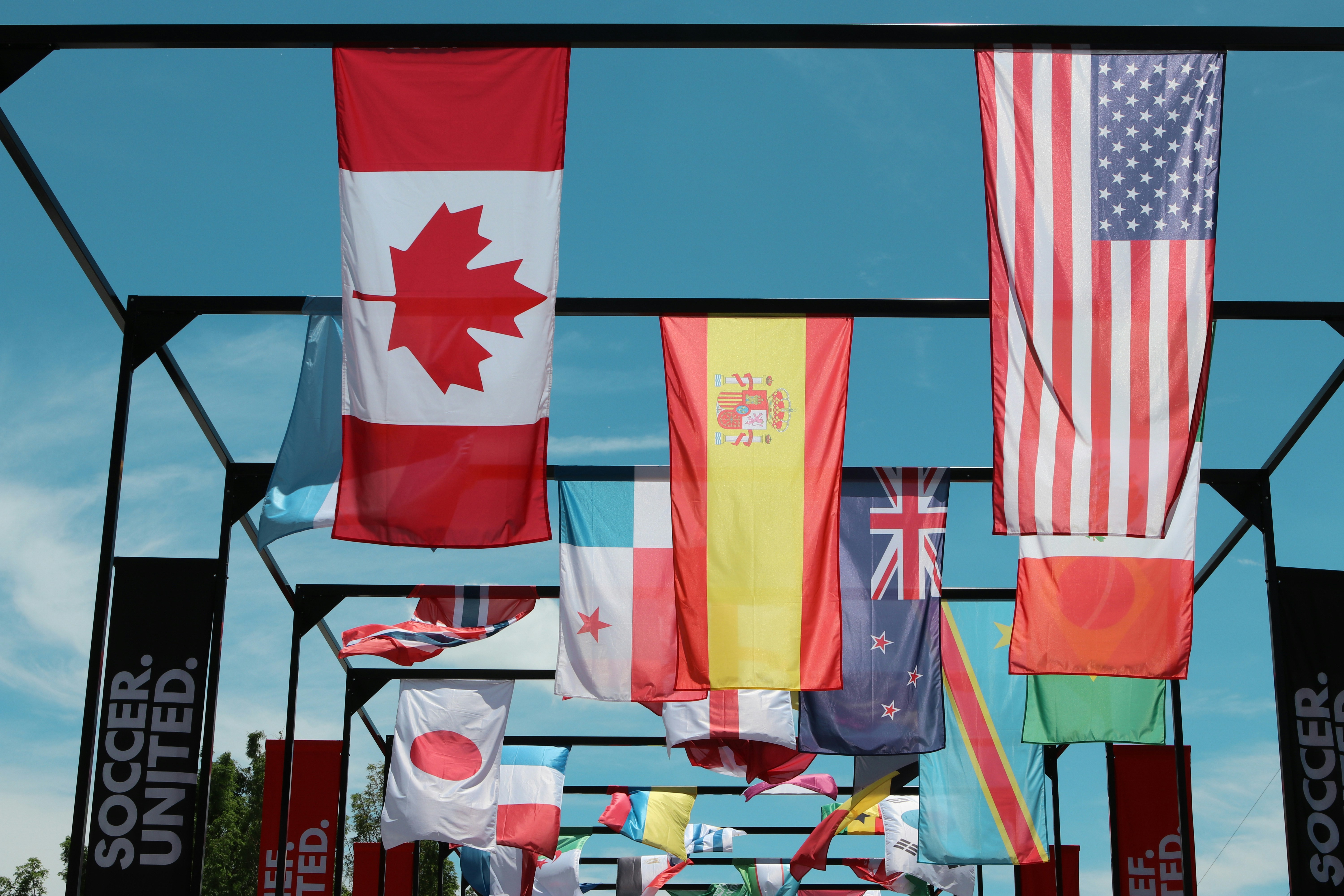 Many national flags suspended from a metal frame outdoors.