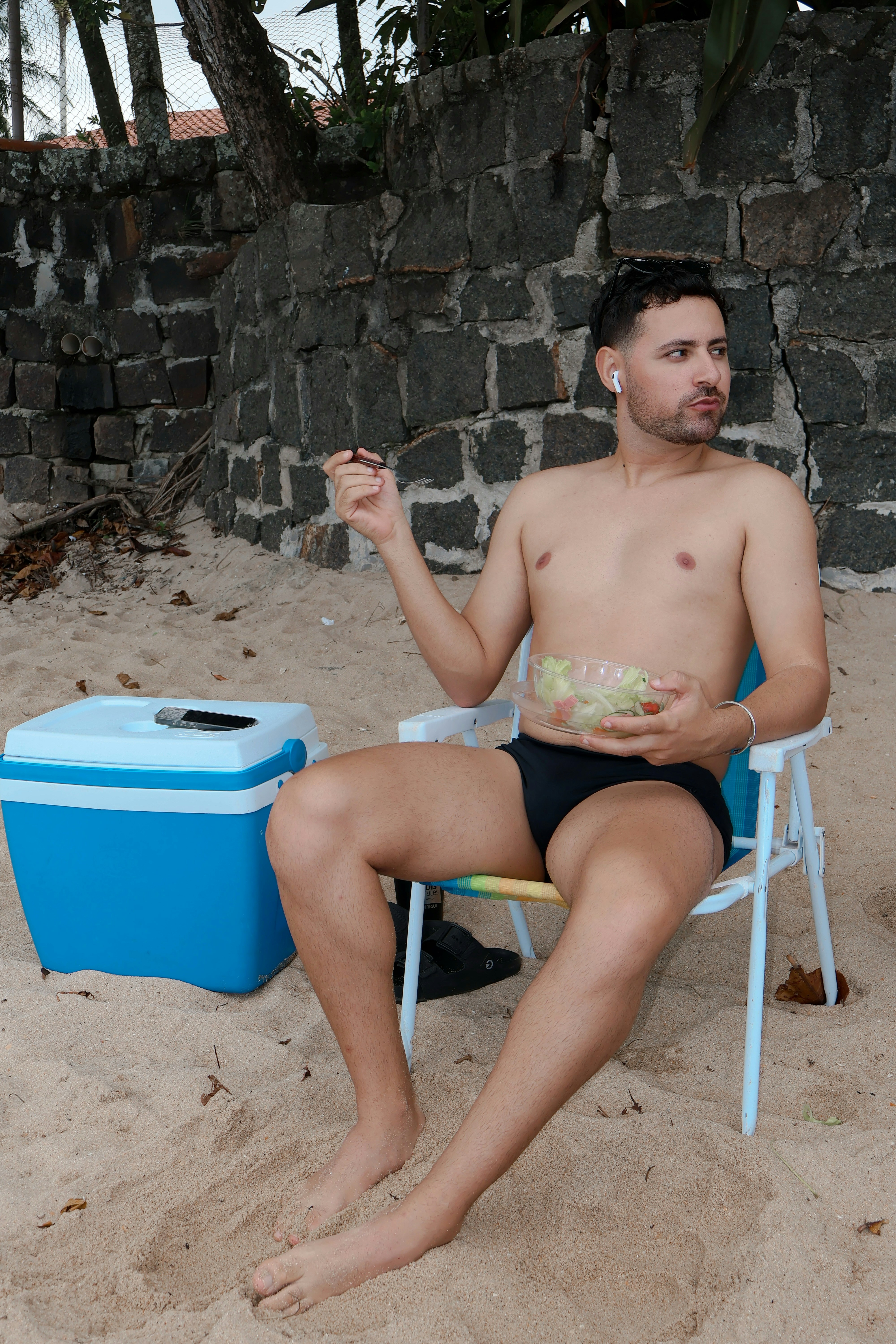 Man eating salad on a beach chair with a cooler.