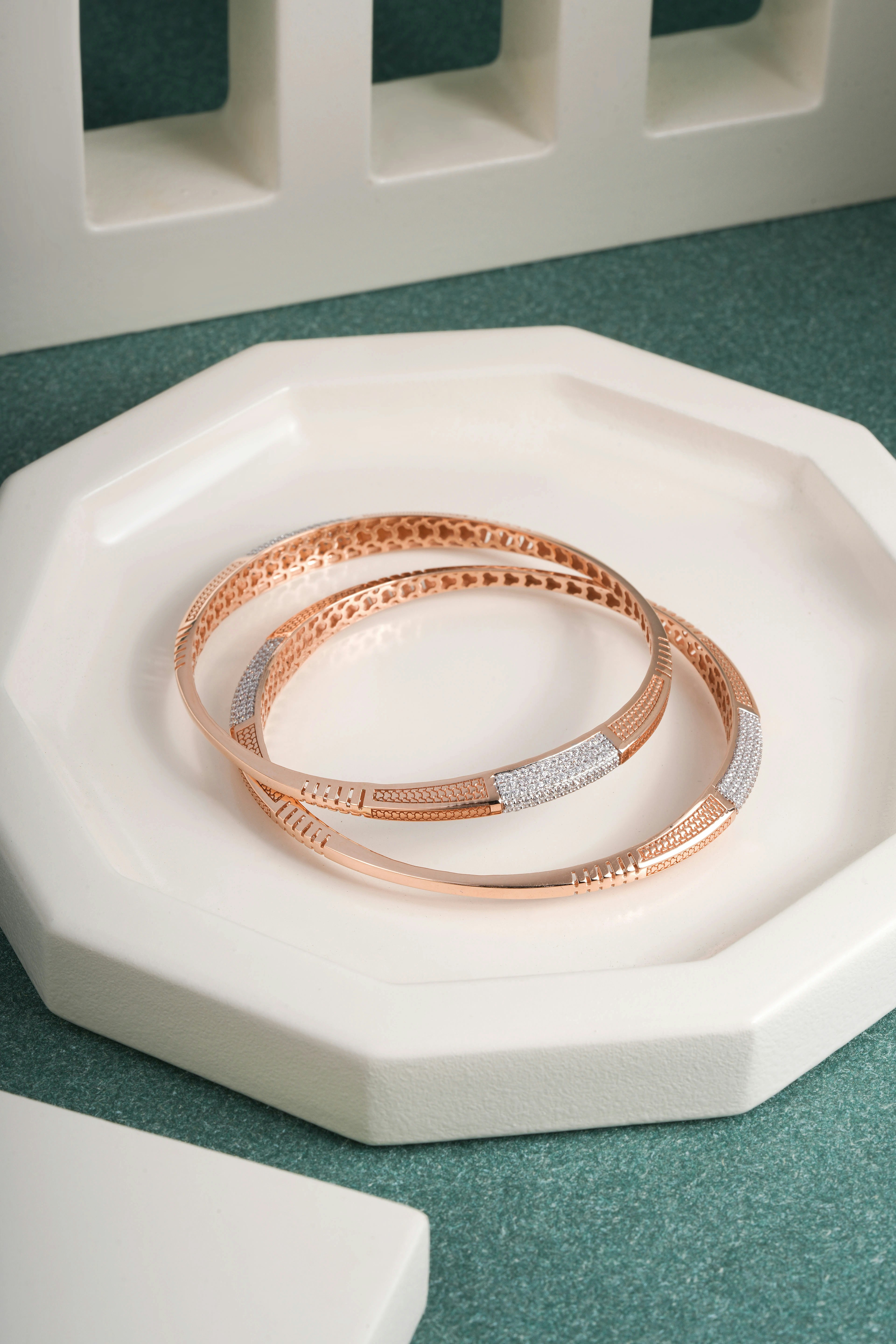 Two rose gold bangles with diamonds on a white tray.