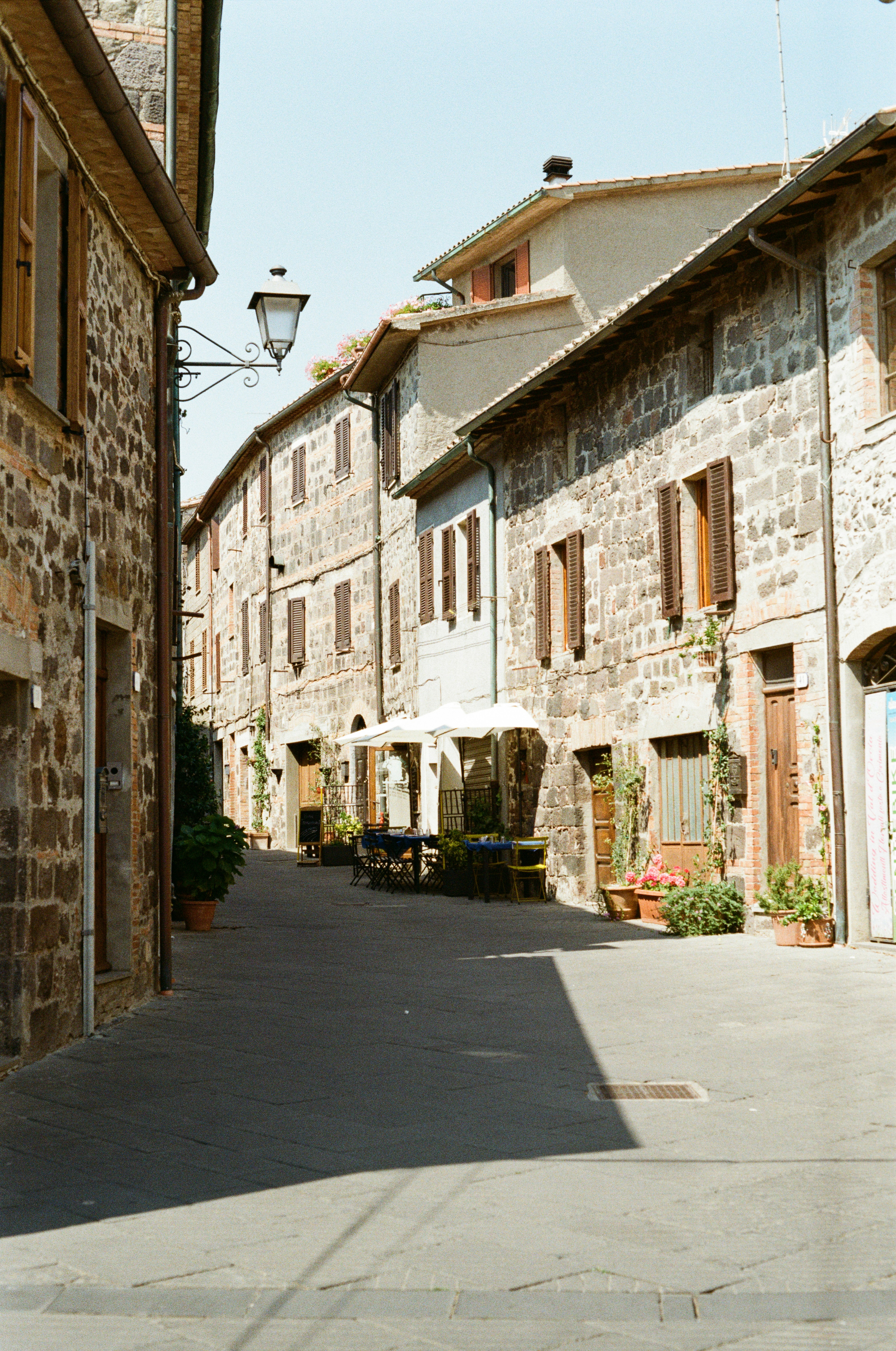 Narrow street with old stone buildings and outdoor dining area.