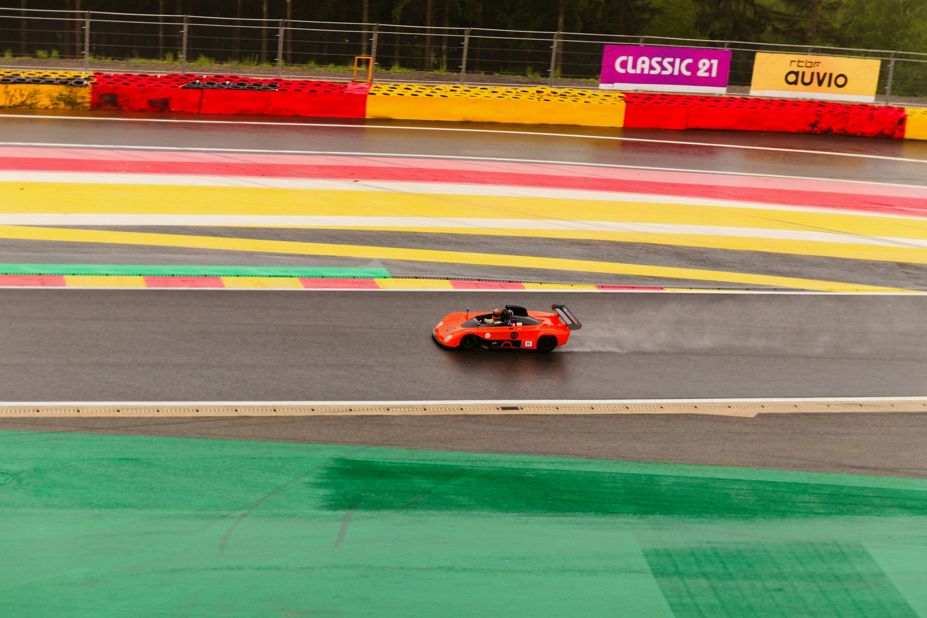 Orange race car on a wet track, spraying water
