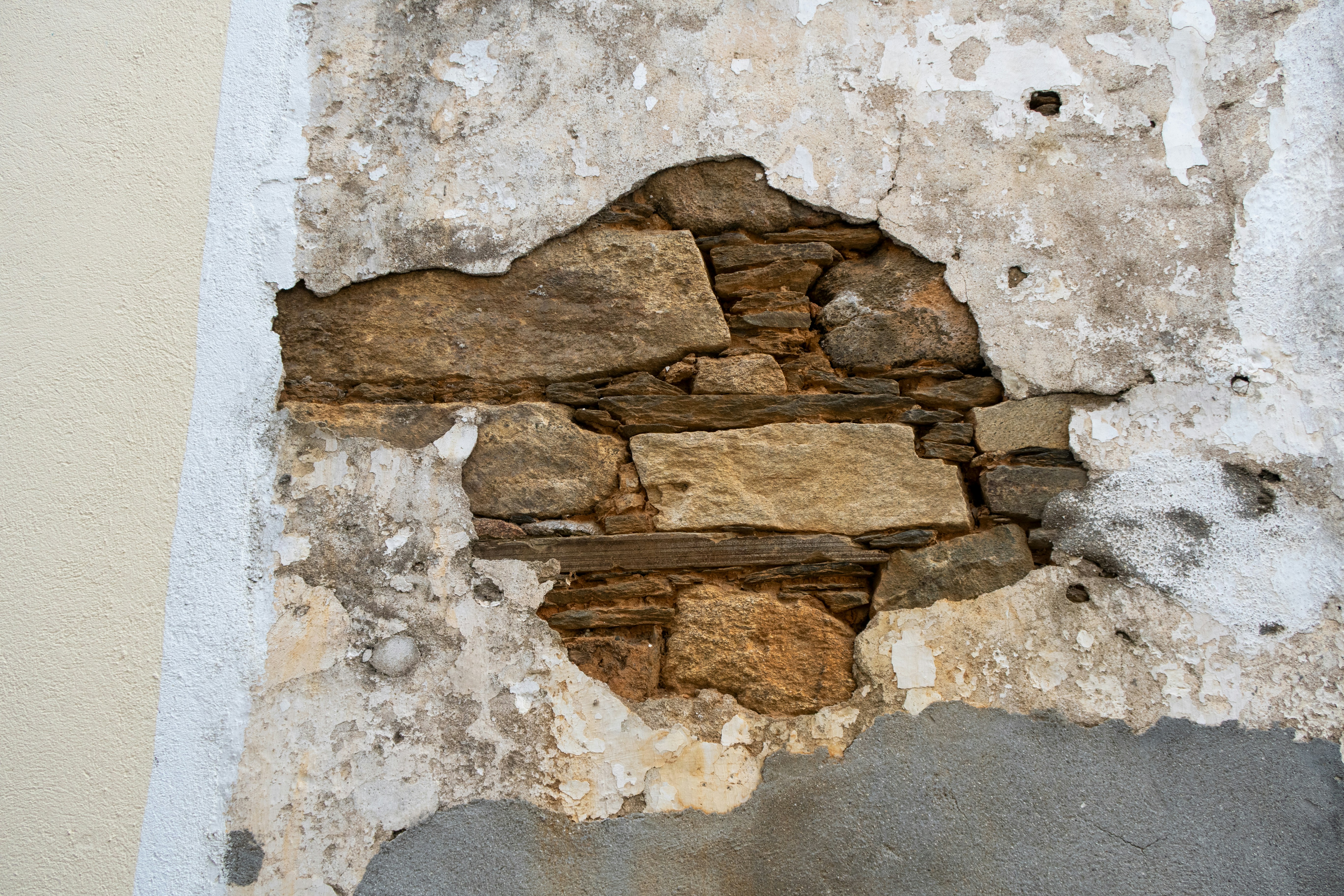 Old plaster peeling from a wall, revealing stone bricks.