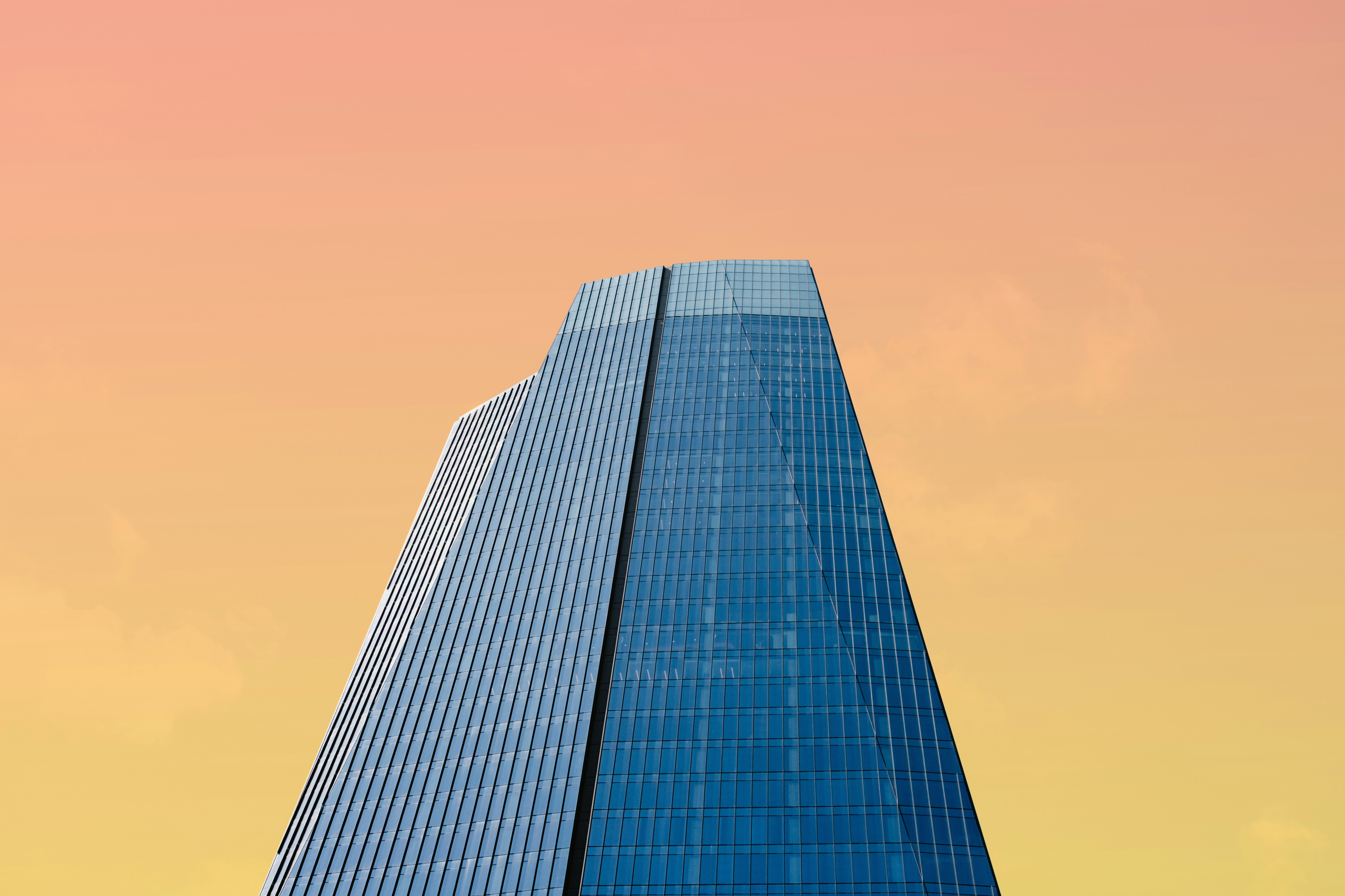 Tall glass skyscraper against orange and yellow gradient sky