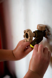 Child's hands touching an outdoor water faucet on a wall