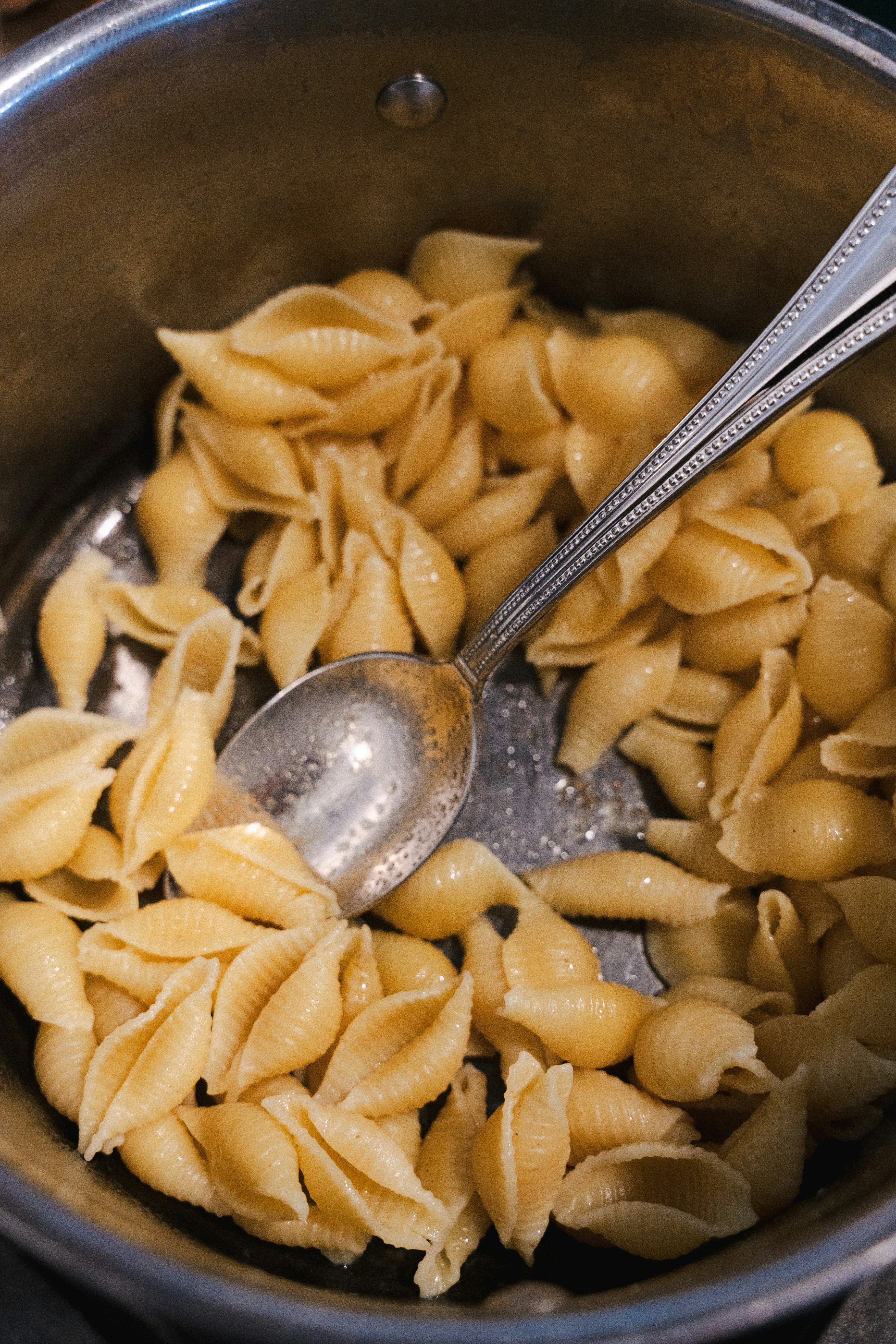 Cooked pasta shells in a pan with a spoon.