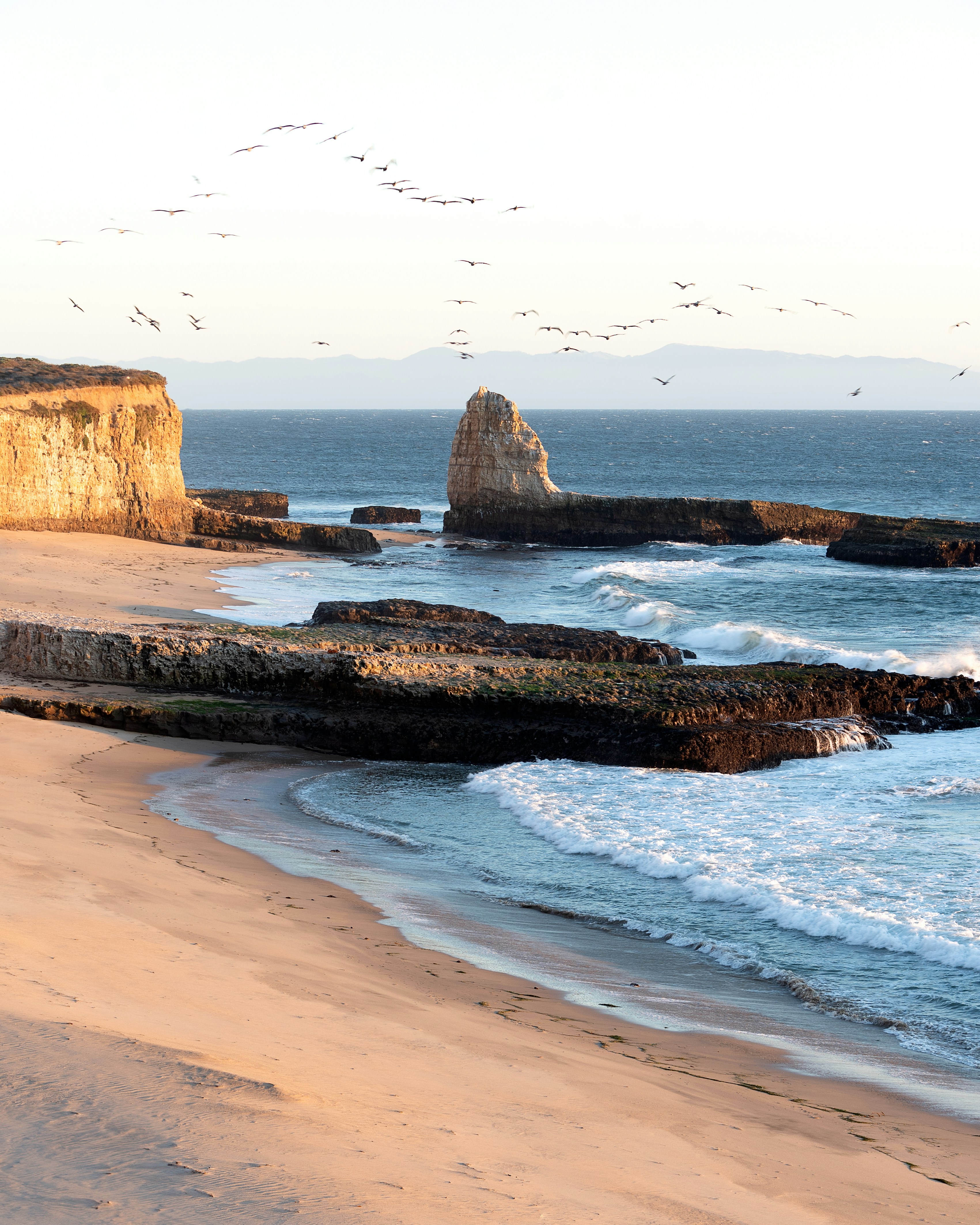 Scenic beach with ocean waves, sea stacks, and towering cliffs.