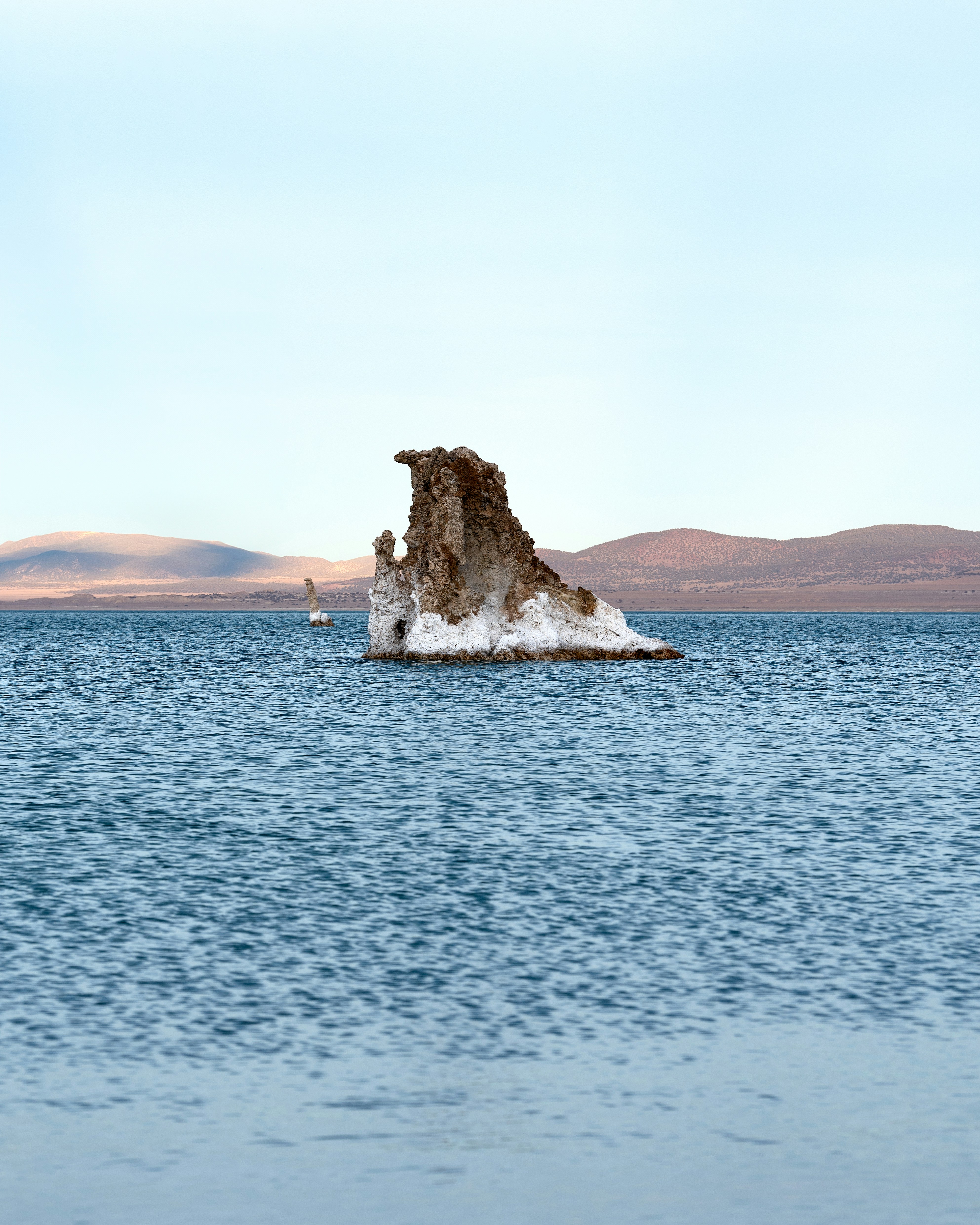 Unique tufa rock formation in a calm lake with hills.