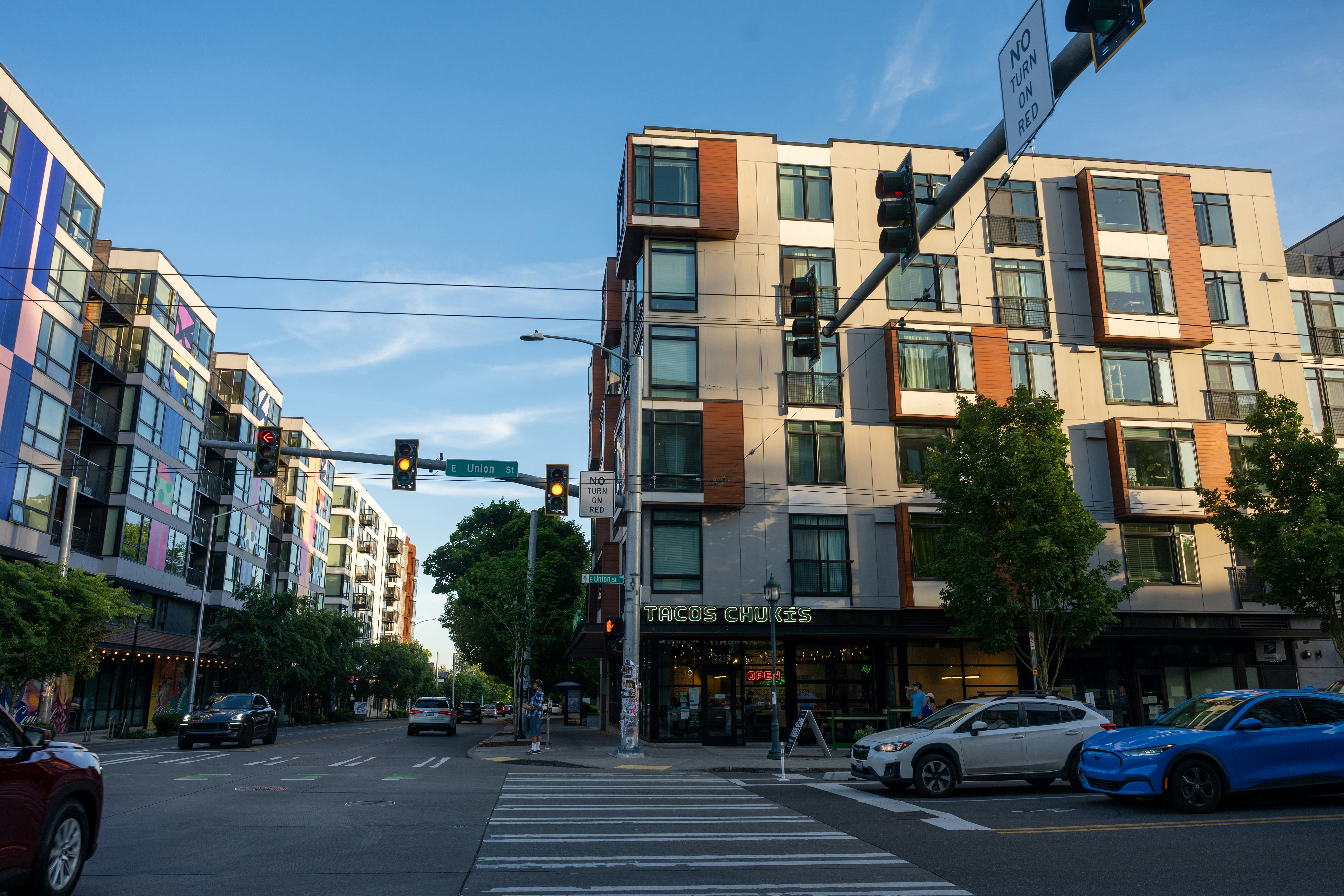 City street with modern buildings, cars, and a pedestrian crosswalk.