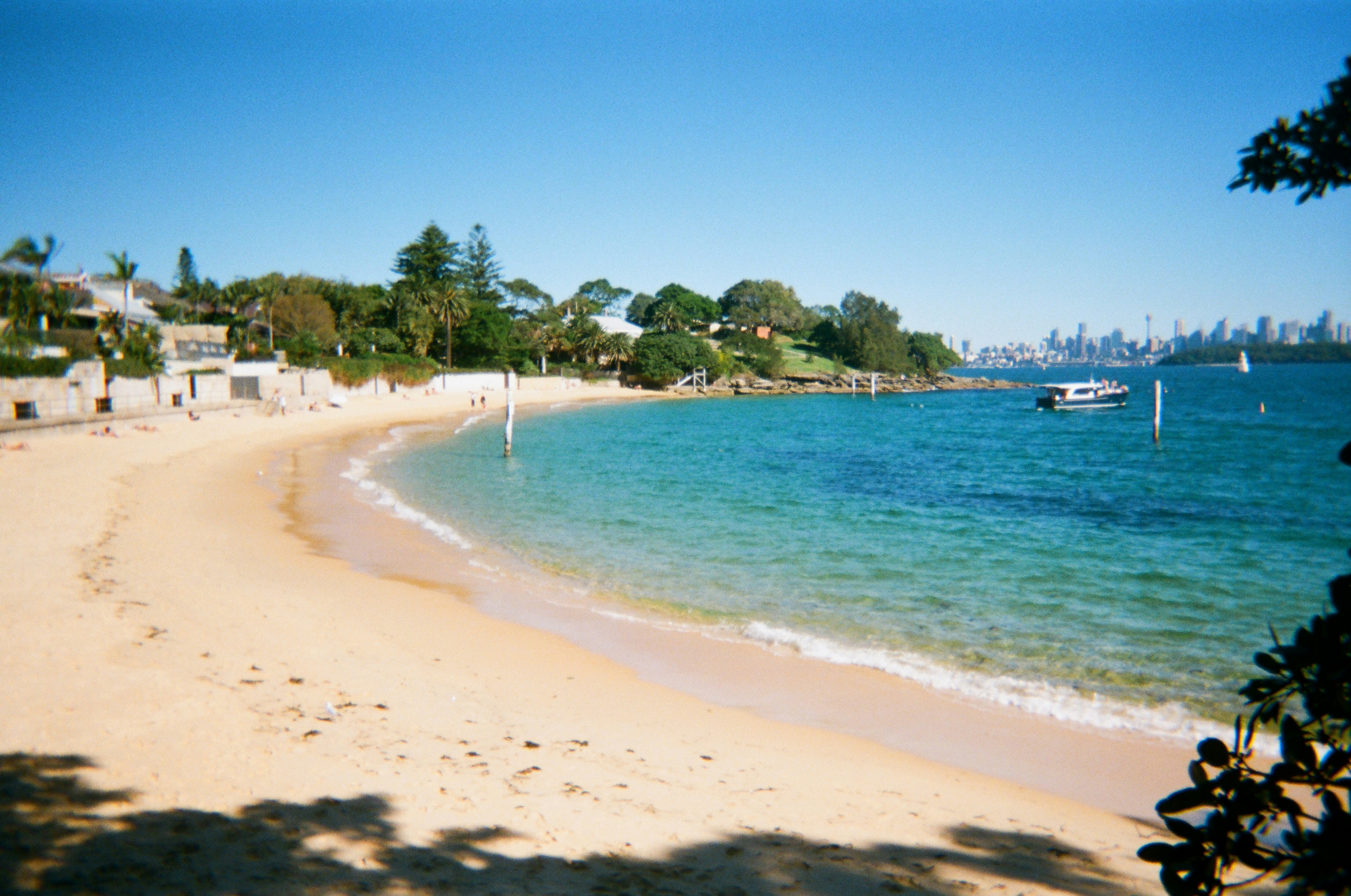 Sandy beach with clear blue water and distant city skyline.