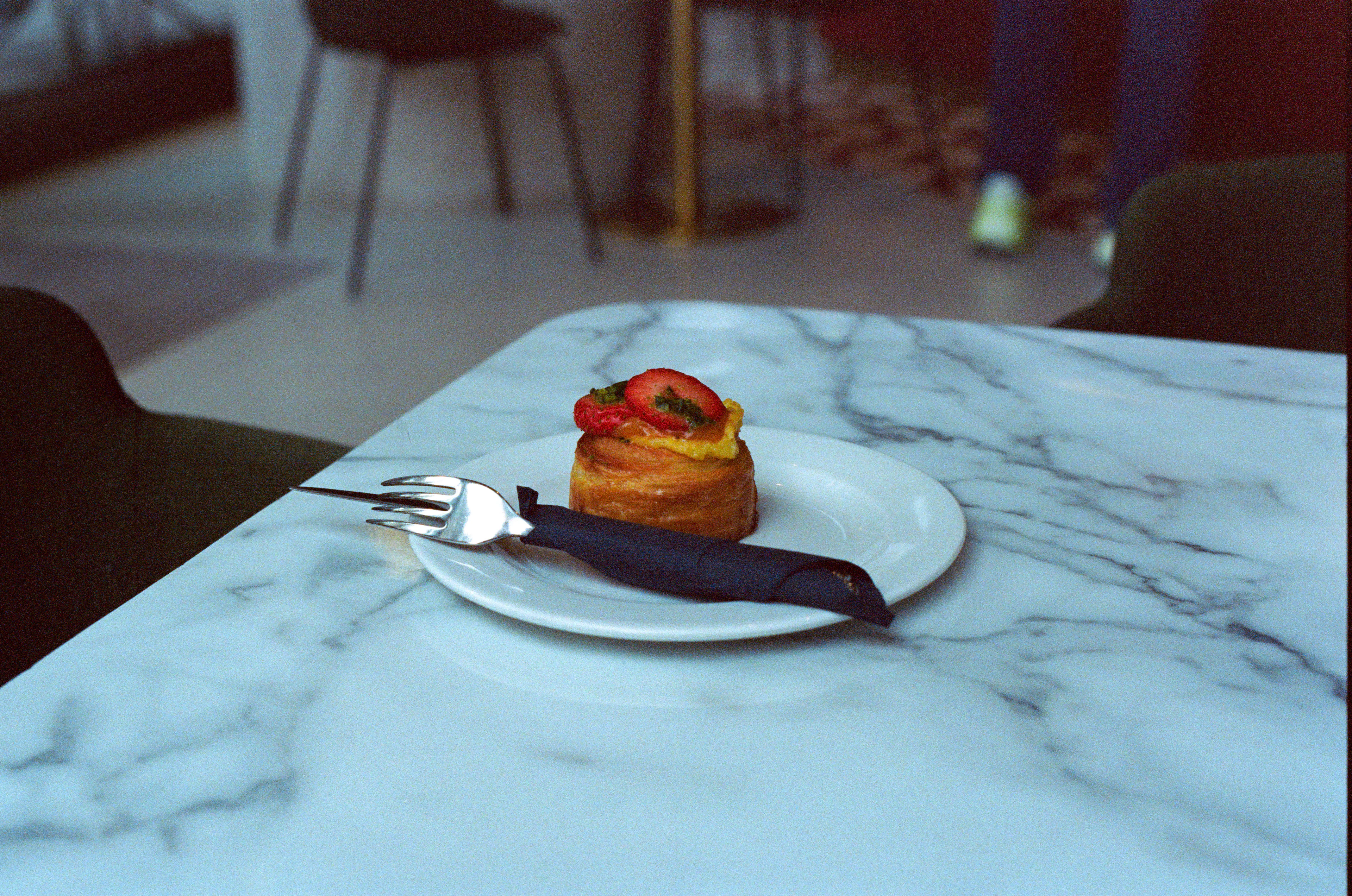 A pastry and a fork on a marble coffeehouse table, a bentwood chair behind it