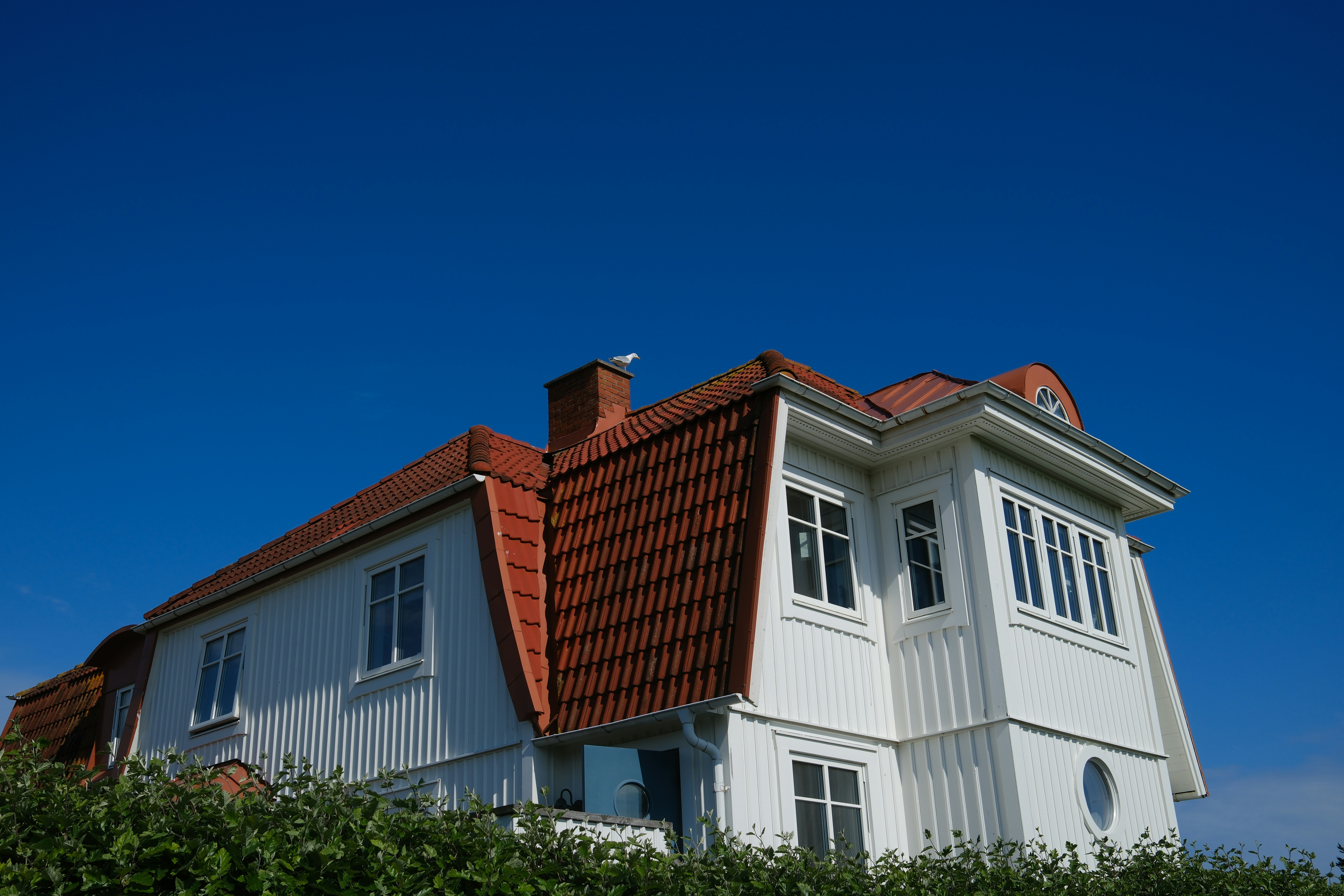 Vit villa med rött tak mot klarblå himmel – typisk uppländsk fastighet lämplig för solceller.
