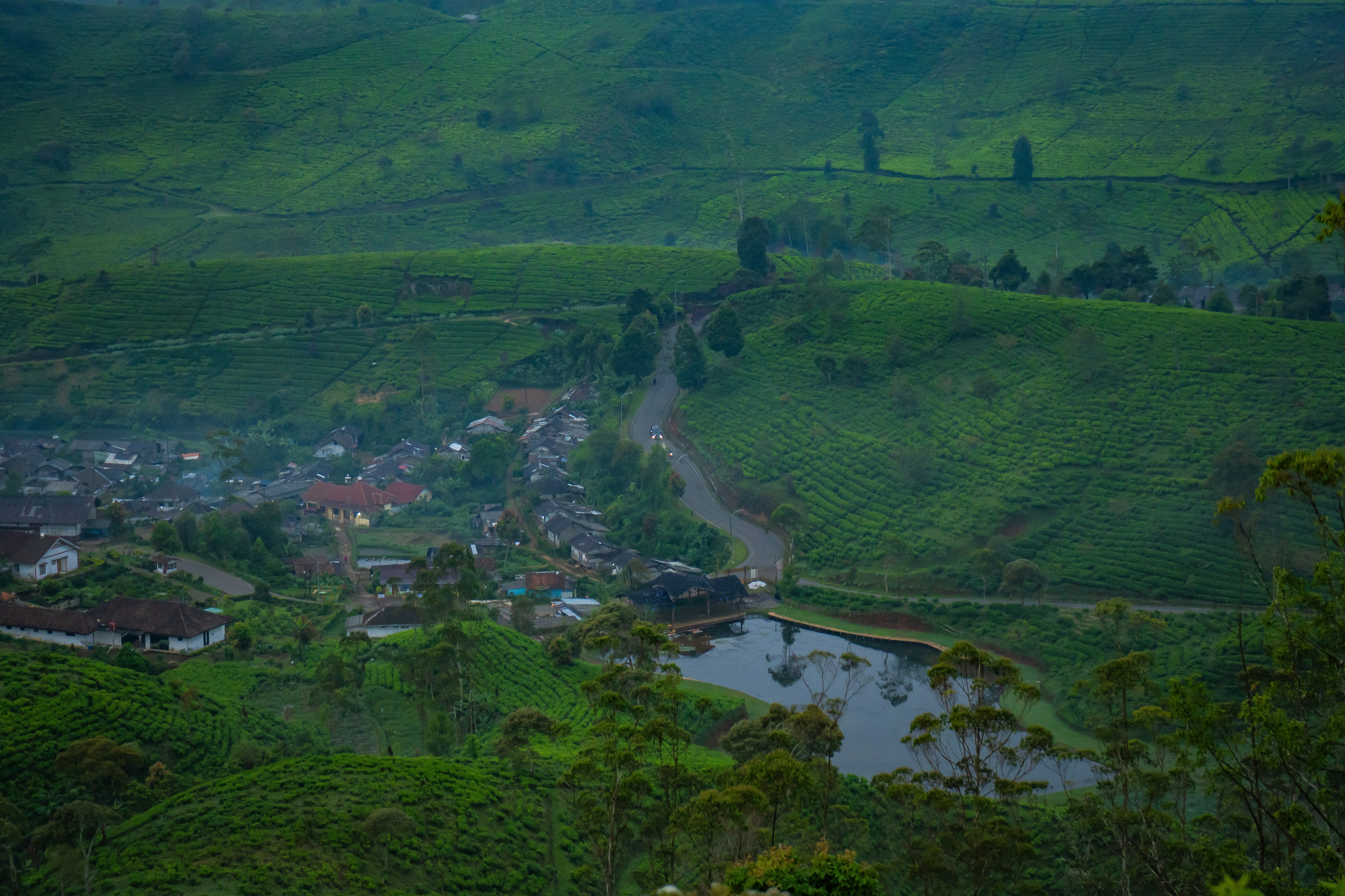 Lush green hills, a village, lake, and winding road.