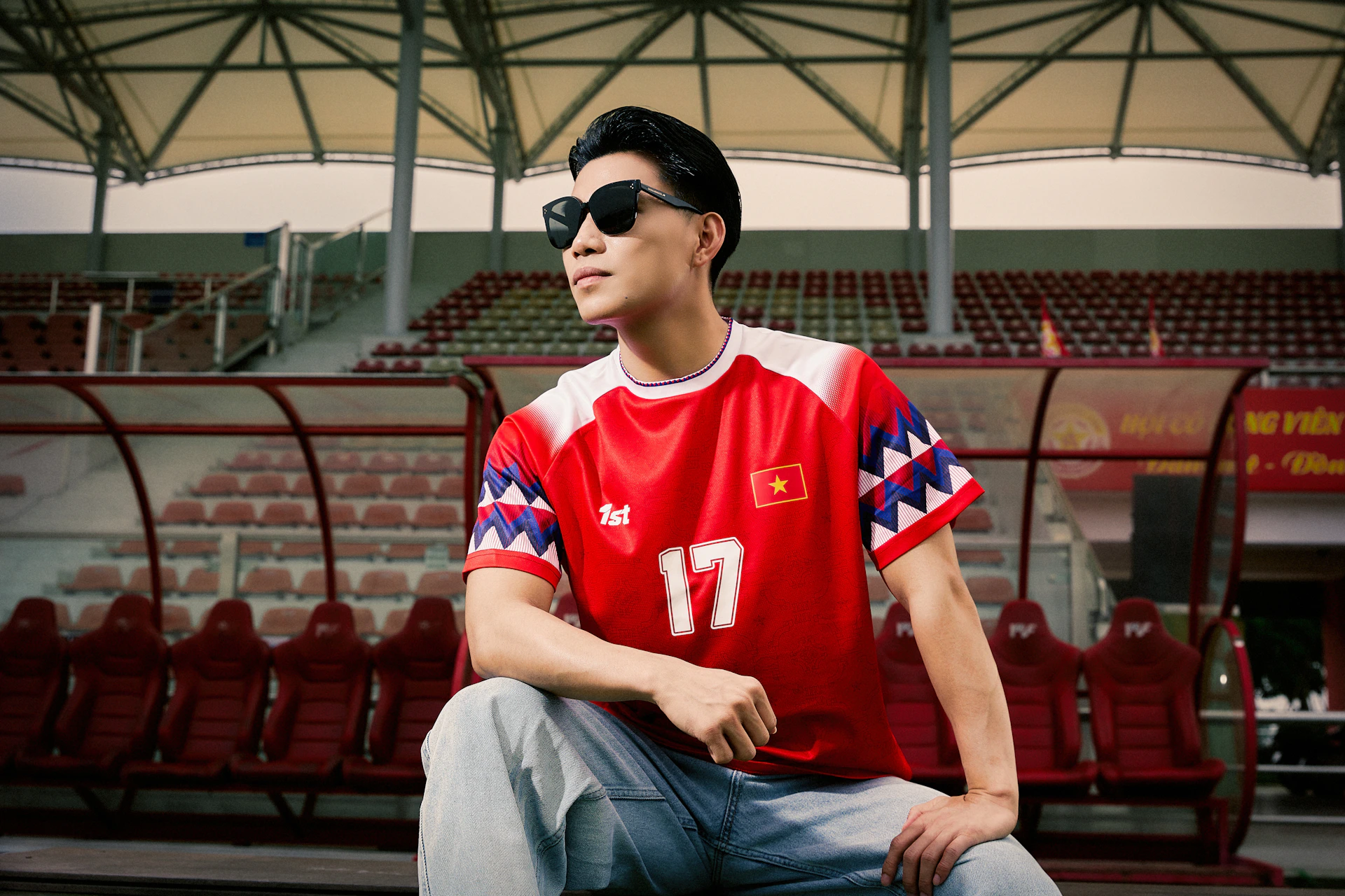 Man in red football jersey and sunglasses sits in stadium