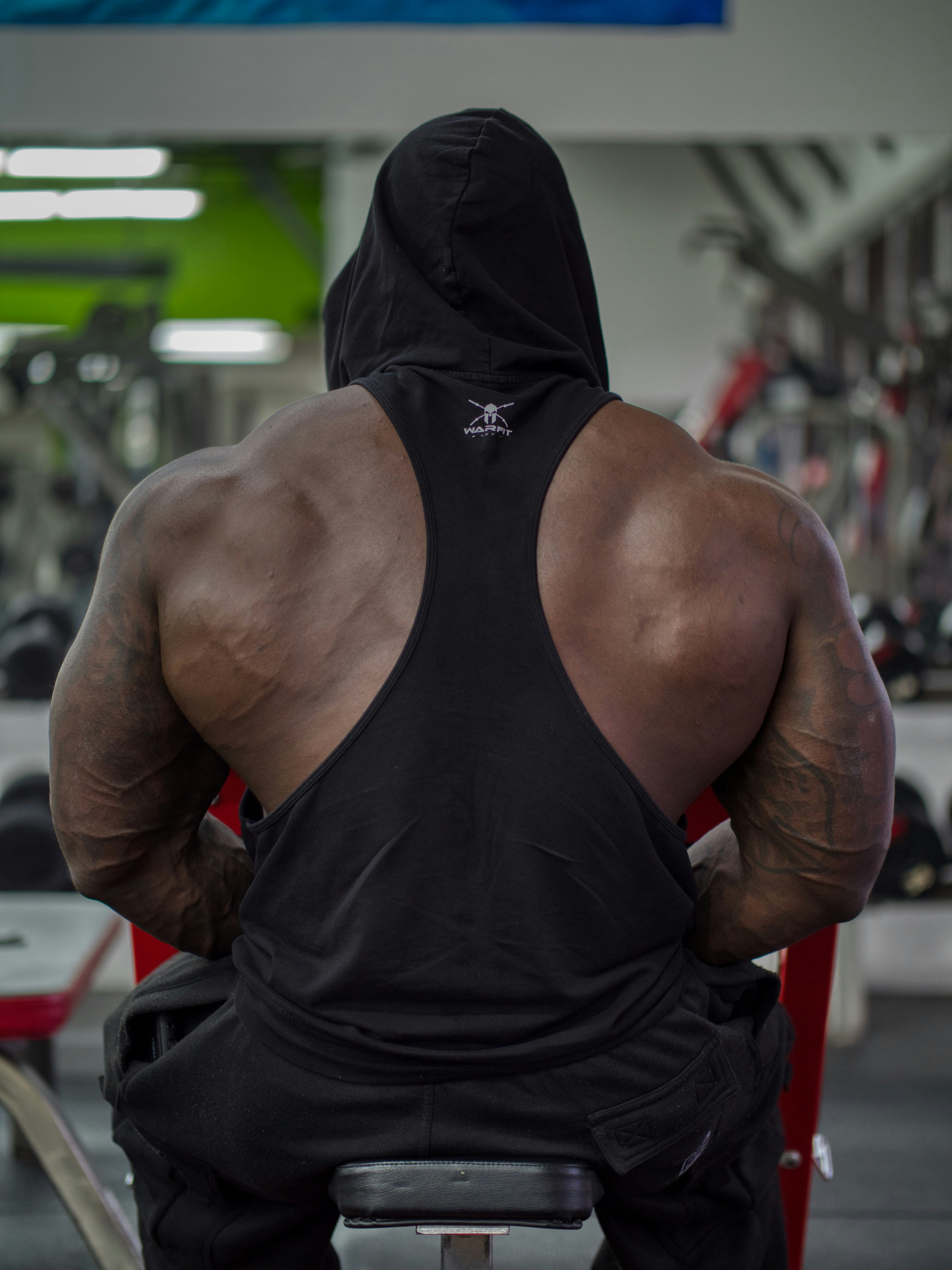 Muscular man in black tank top sitting in gym.