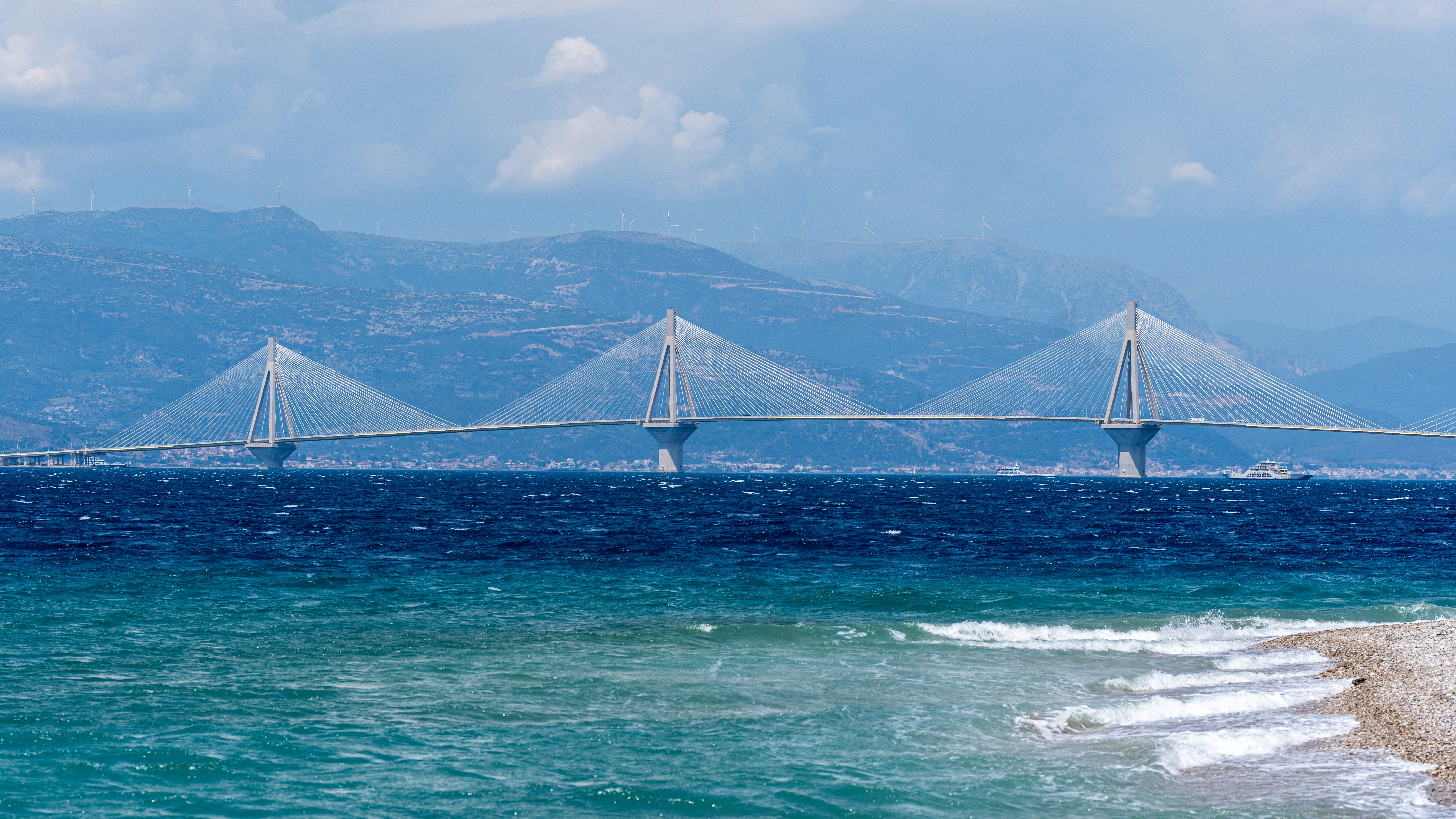 Modern cable-stayed bridge spans blue water with distant mountains