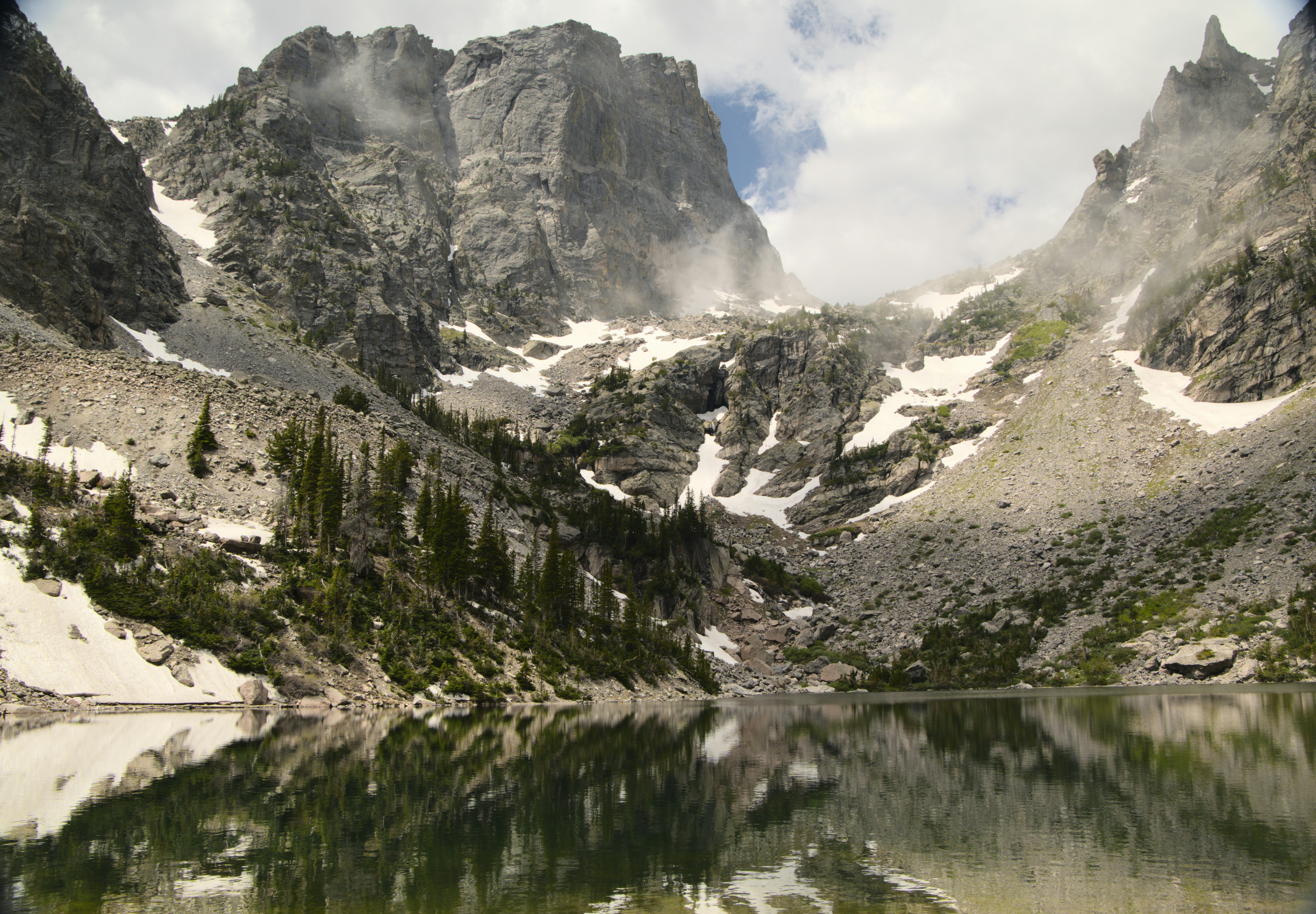 Serene mountain lake reflecting snowy peaks and evergreen trees.