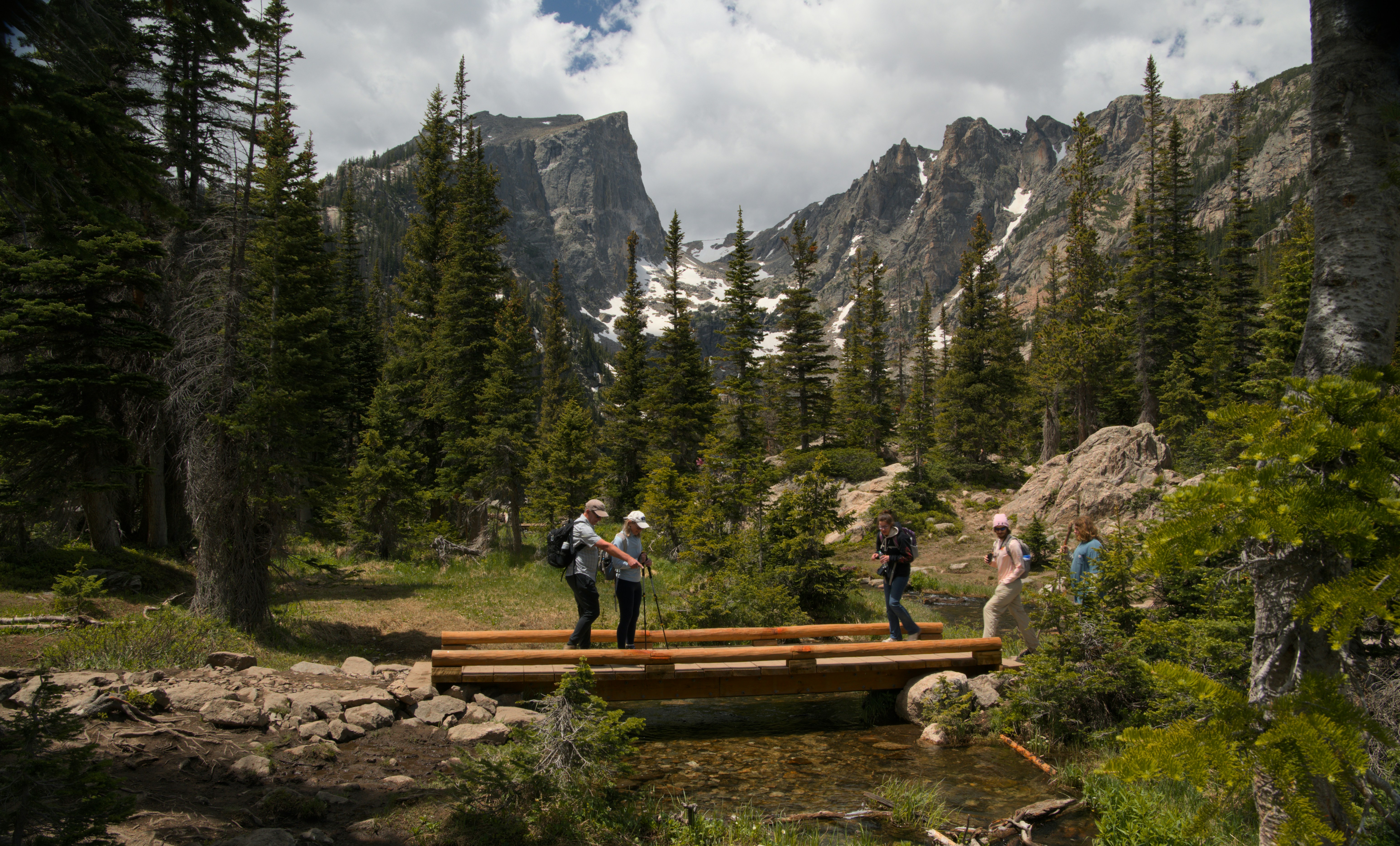 Hikers cross a wooden bridge in a mountain forest.