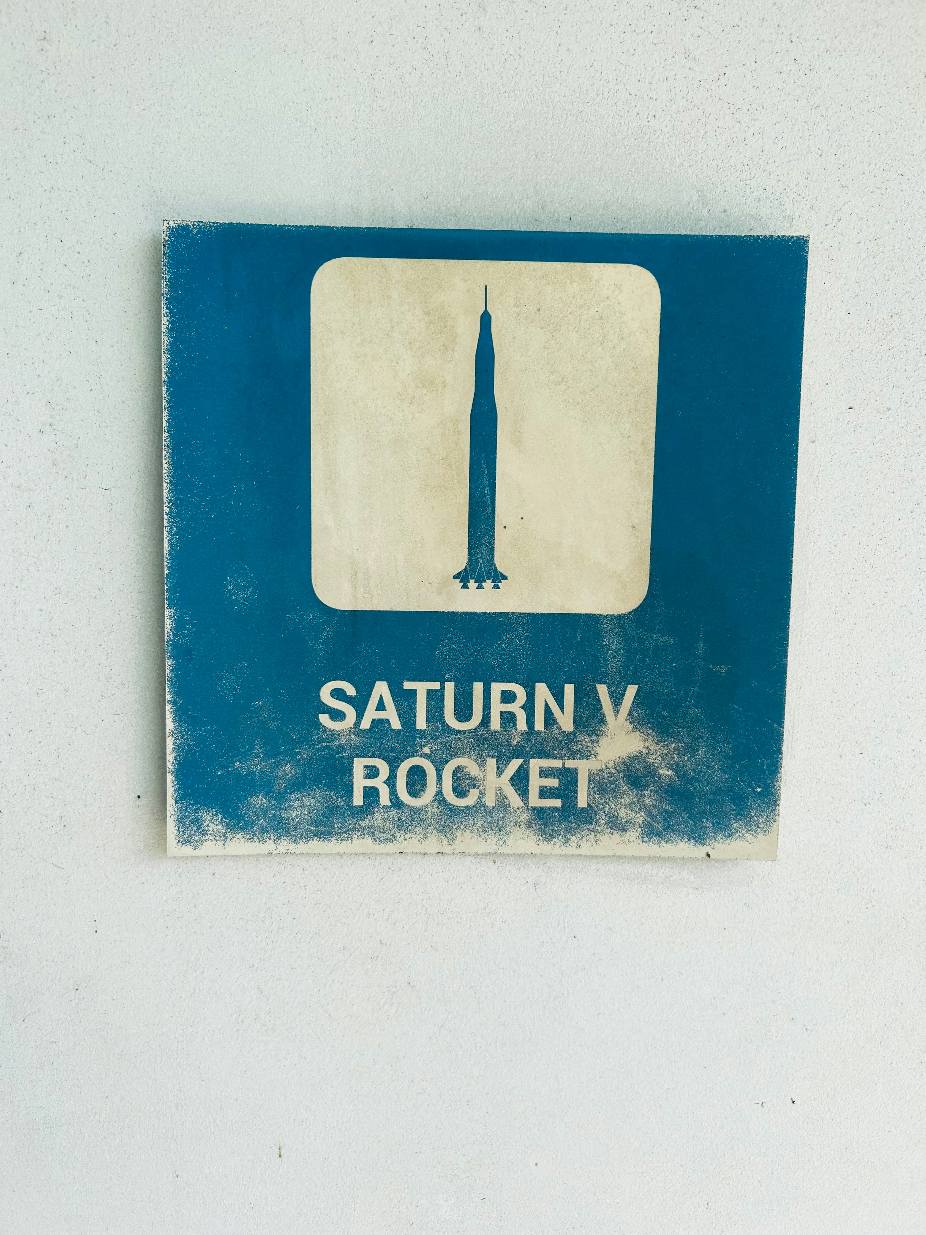 Uma placa azul desgastada com a silhueta do Saturn V.
