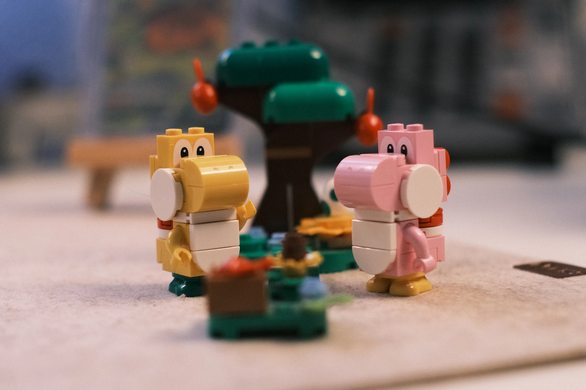Two lego yoshi figures and a tree on a table.