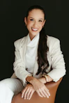 Smiling woman in white blazer sitting in a chair.