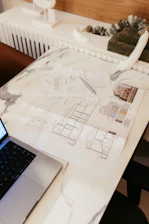 Architectural blueprints and a laptop on a marble desk.