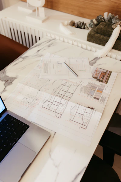 Architectural blueprints and a laptop on a marble desk.