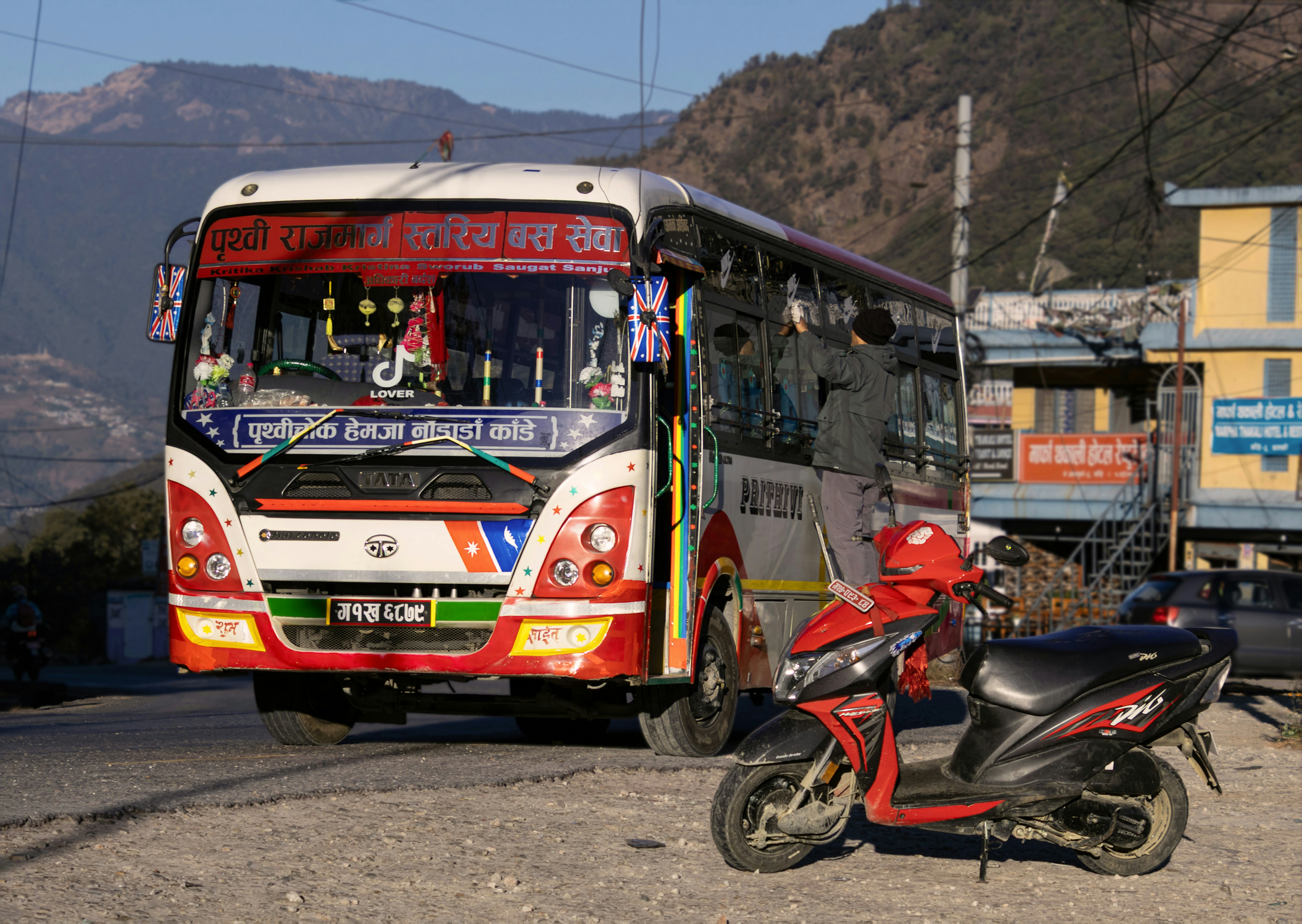 Bus warna-warni dan skuter merah di jalan pegunungan.