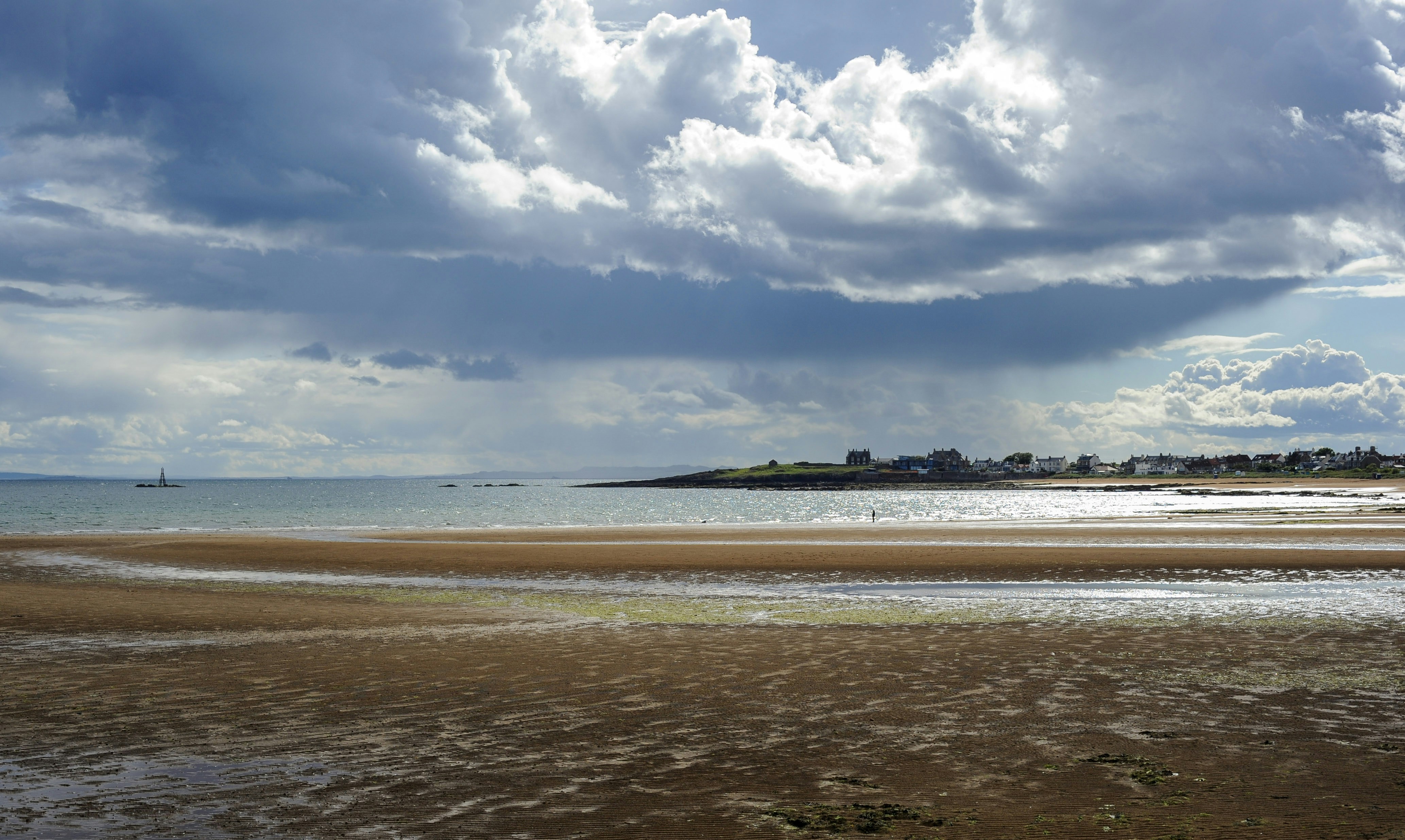 Expansive beach at low tide under a dramatic cloudy sky.