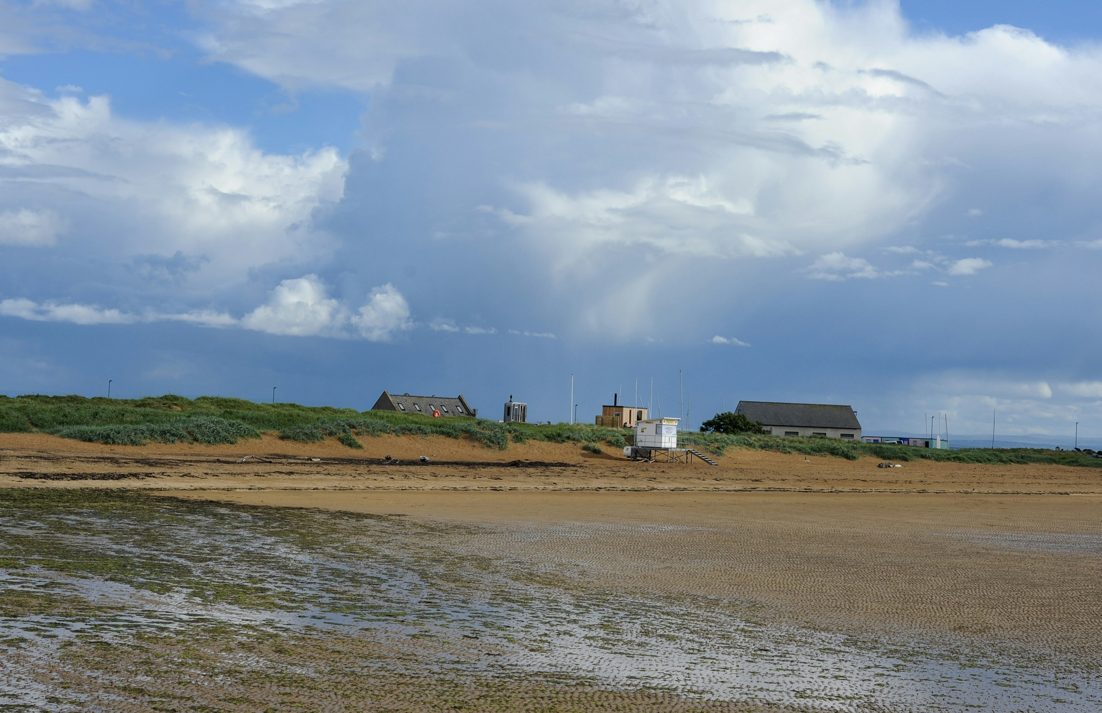 Buildings on a grassy dune under a dramatic cloudy sky.