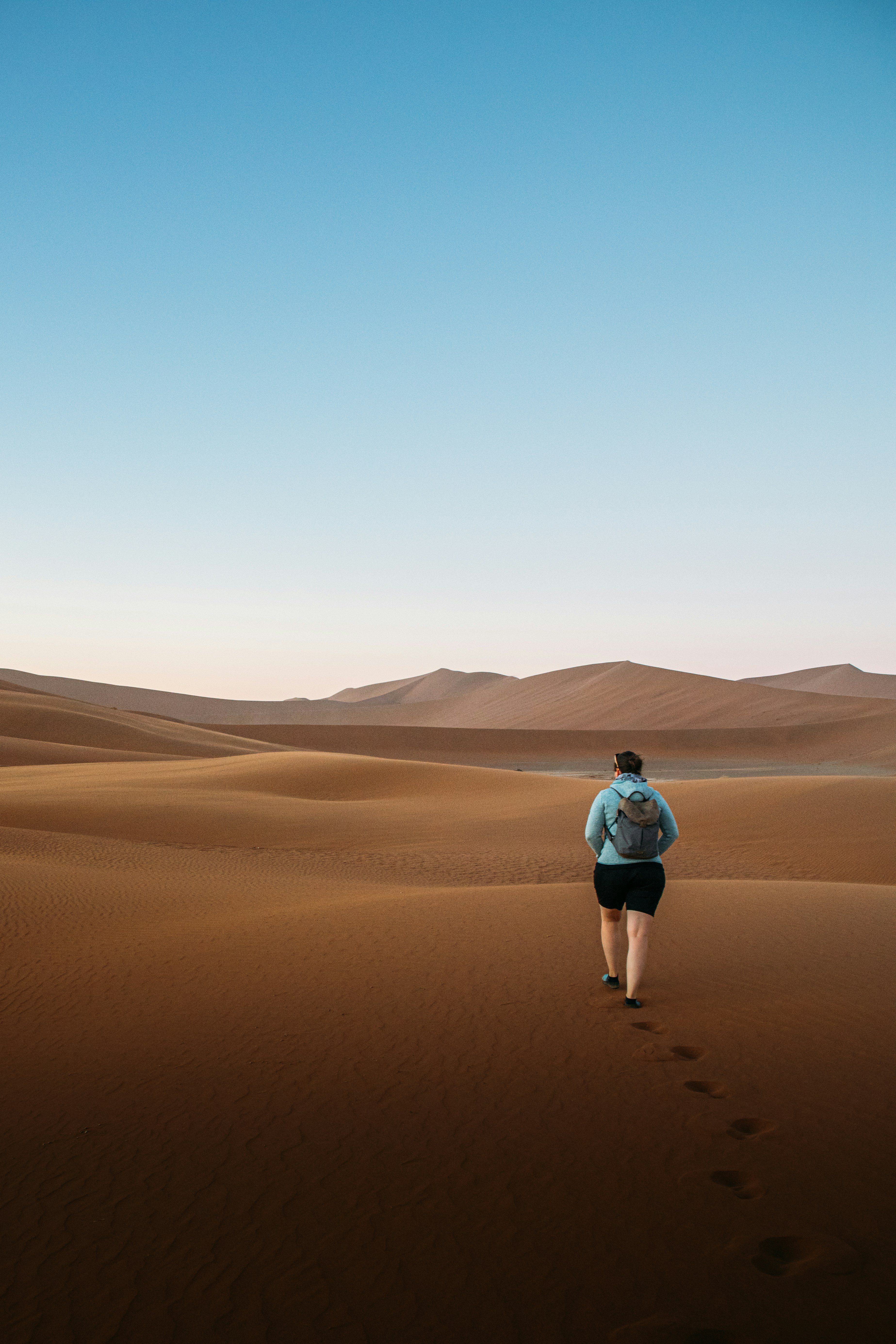 Hiker with backpack walks across desert sand dunes
