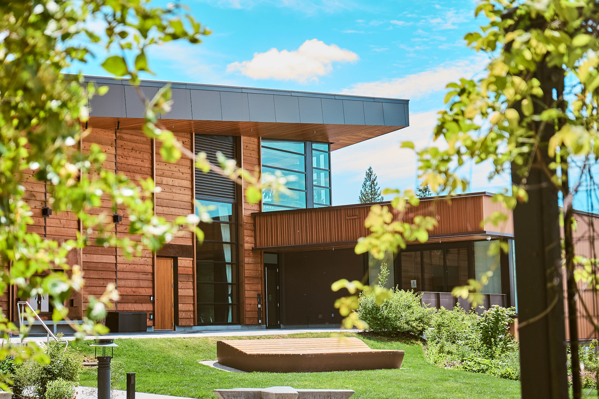 A modern building with wood siding surrounded by green trees.