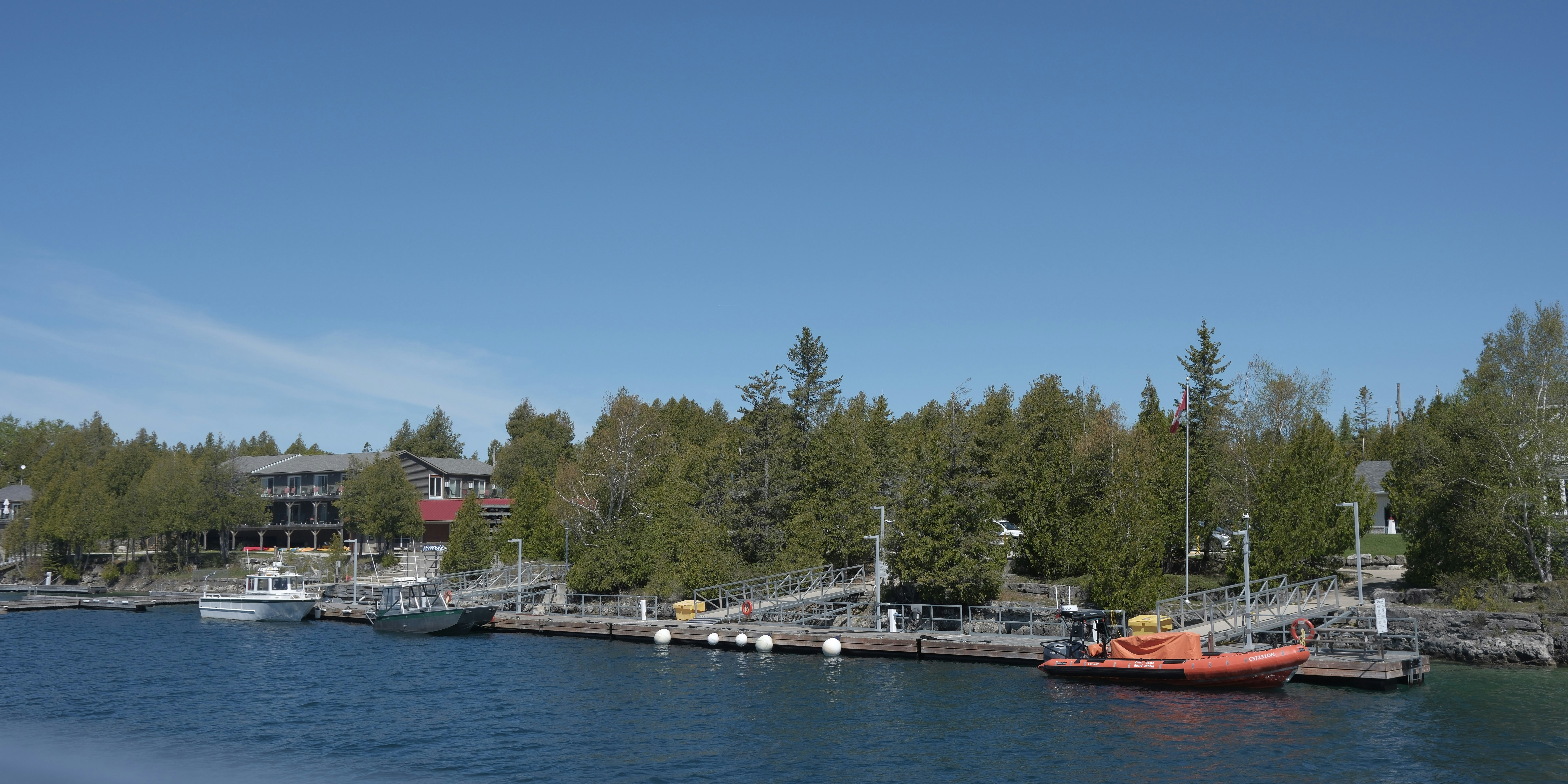 Waterfront with boats, docks, green trees, and distant buildings.