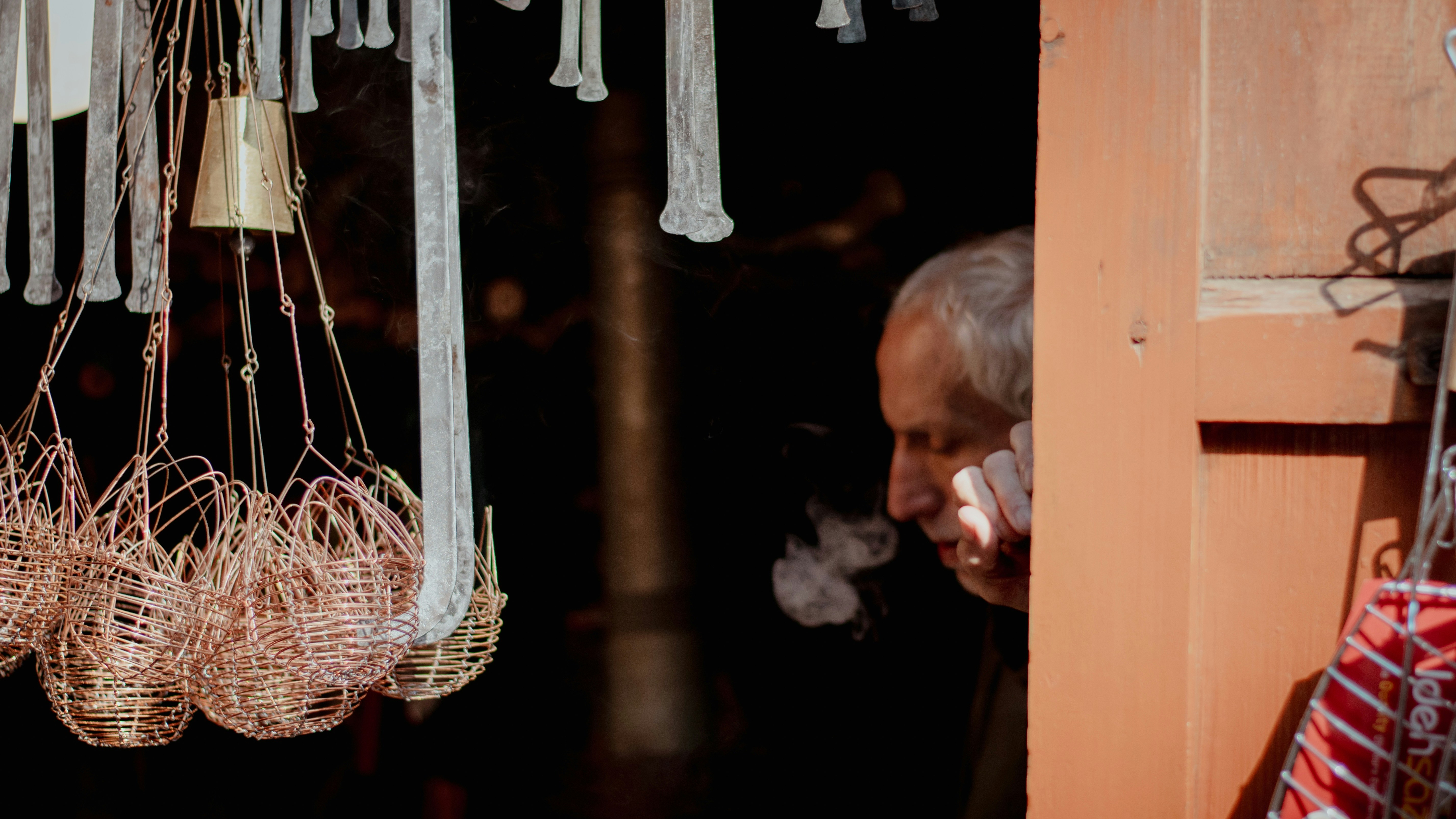 A man smoking a cigarette near hanging baskets.