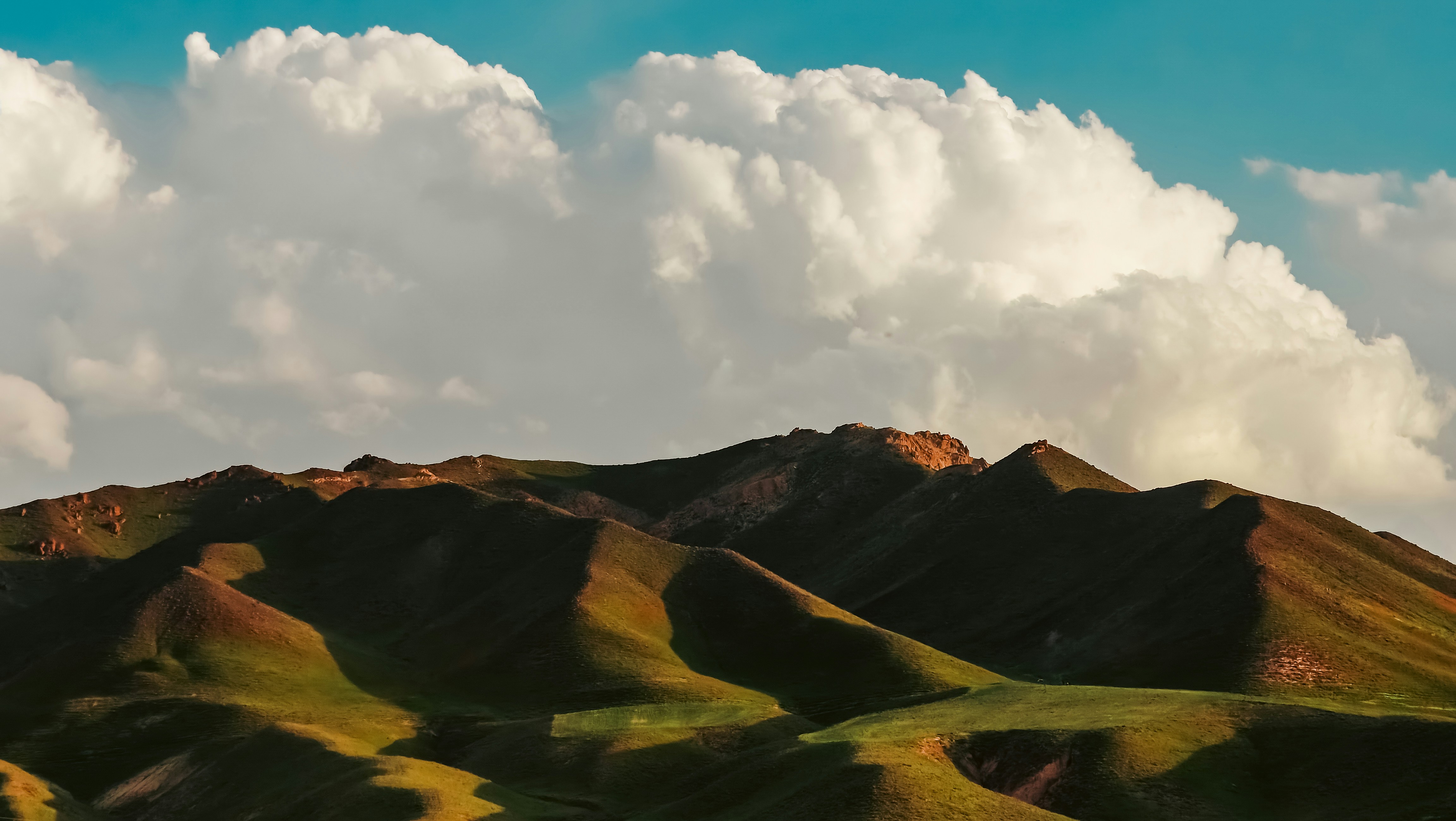Green hills and mountains under a cloudy blue sky.