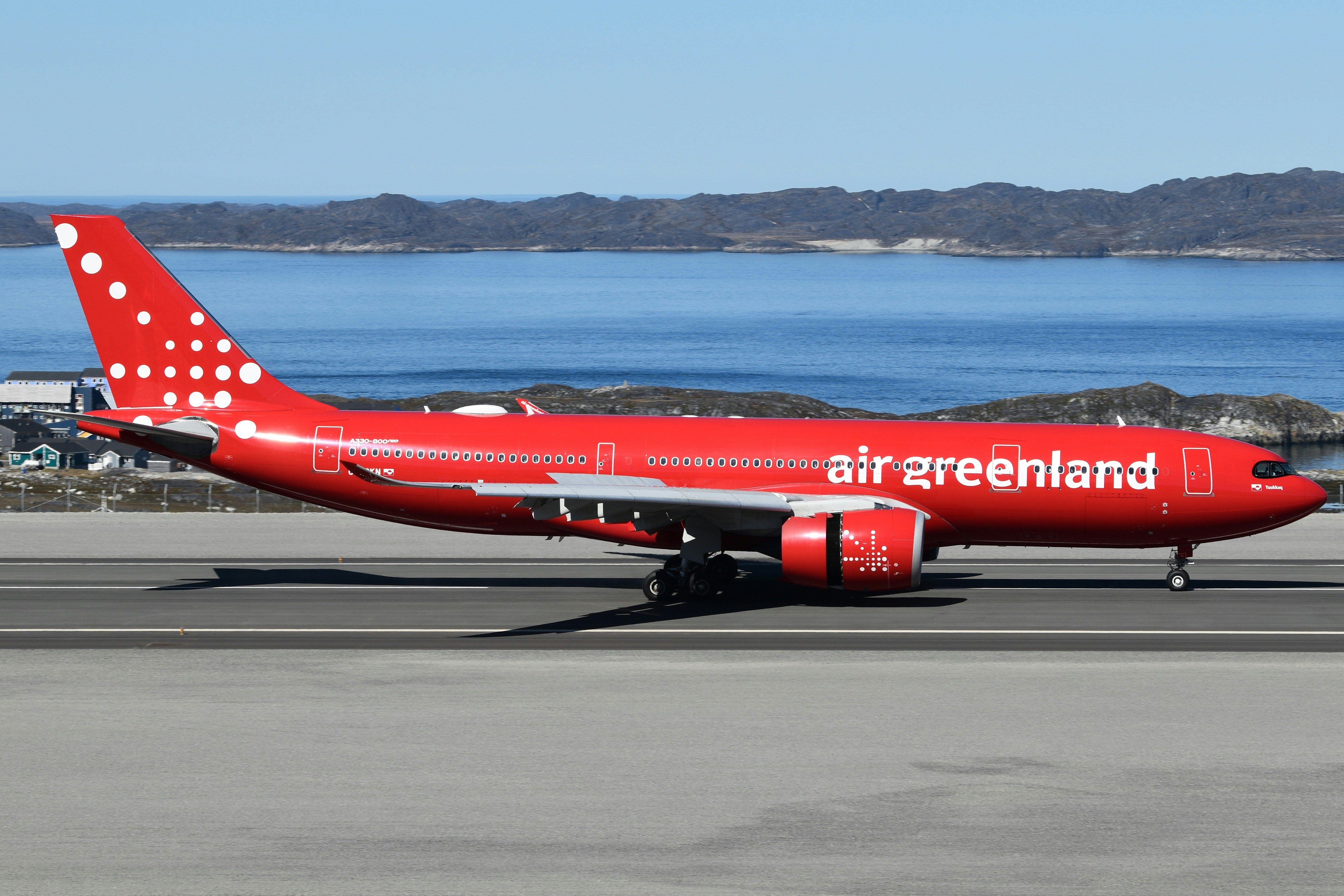 A red air greenland airplane on a runway near water.