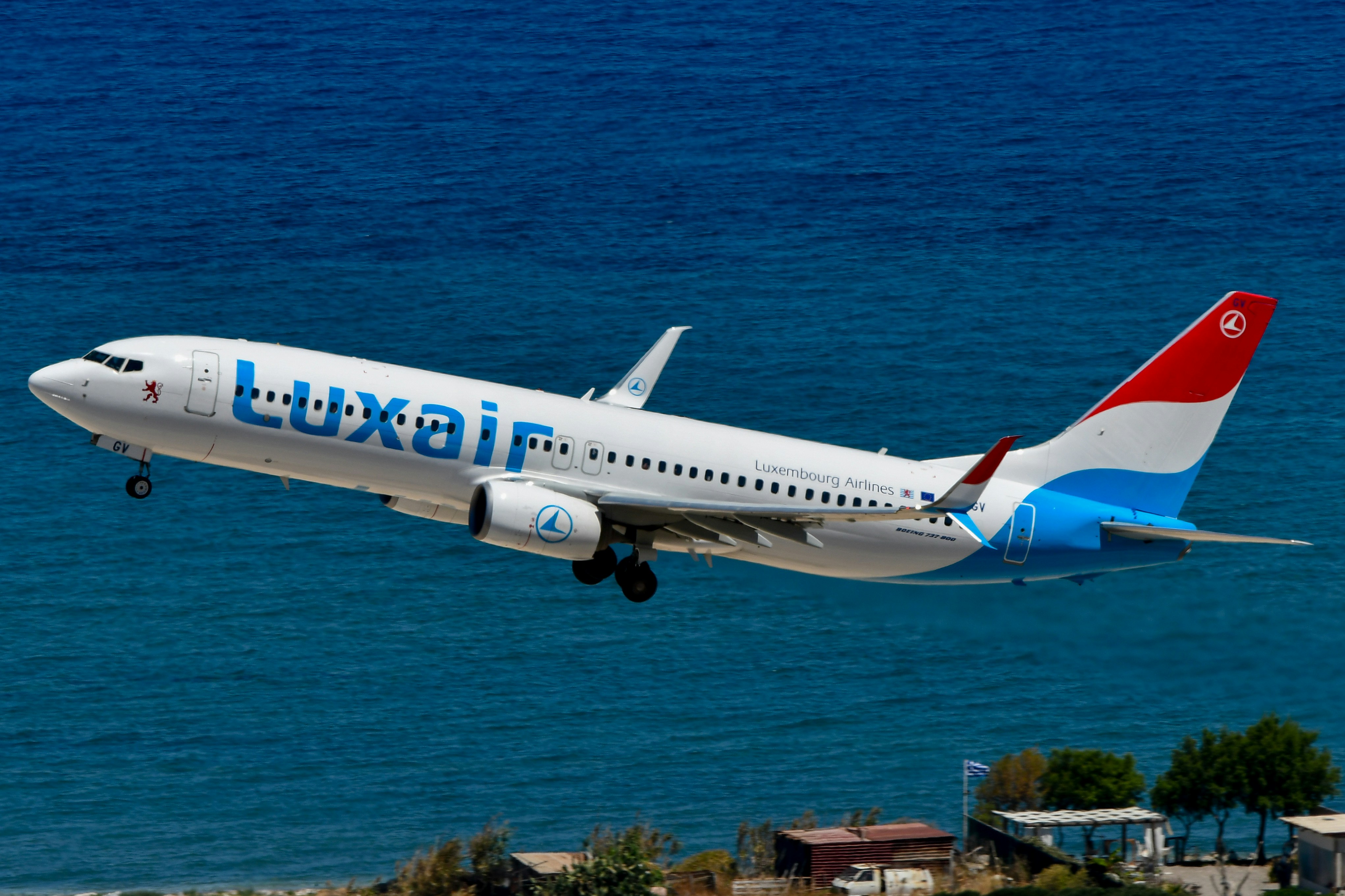 A luxair airplane takes off above the blue ocean.