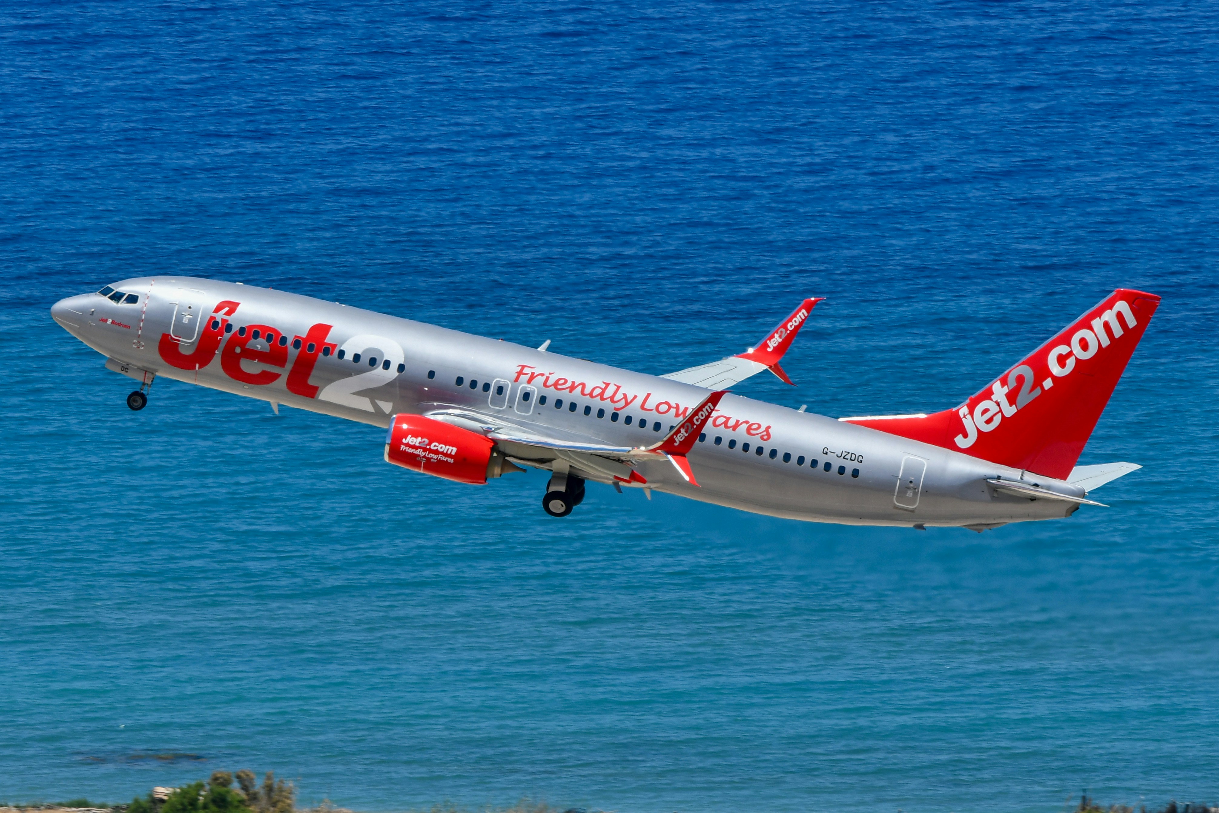 Jet2.com airplane taking off over blue ocean.