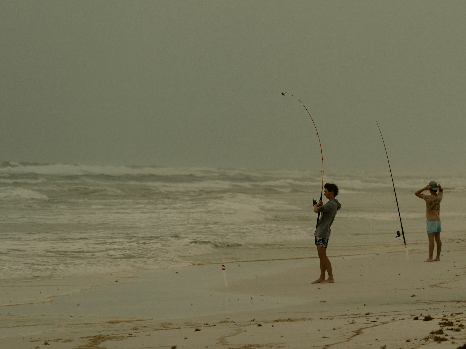 Two anglers surf fishing from a sandy ocean beach